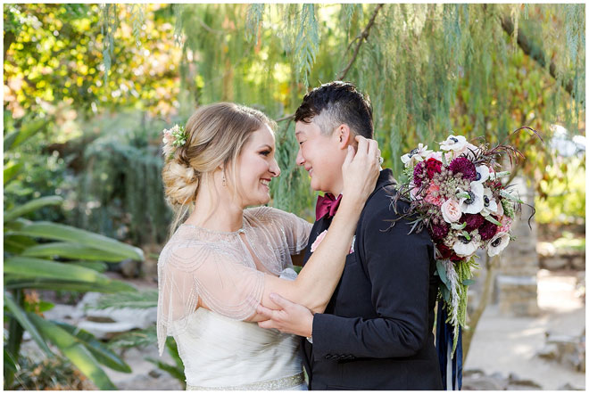 Bride and Bride hold each other face to face in a garden.