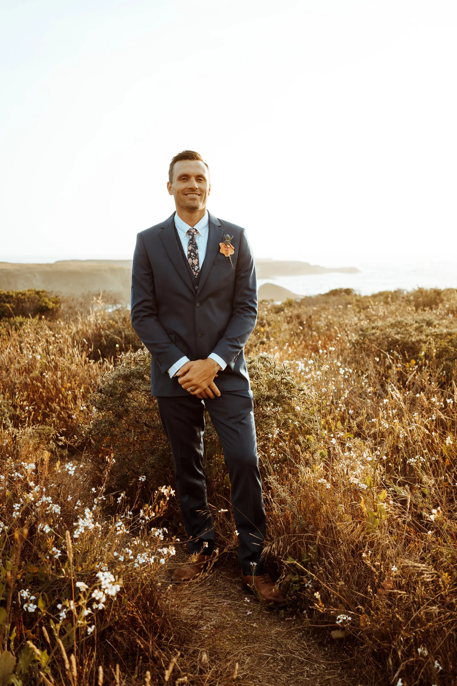 Groom posing for photo in field of flowers