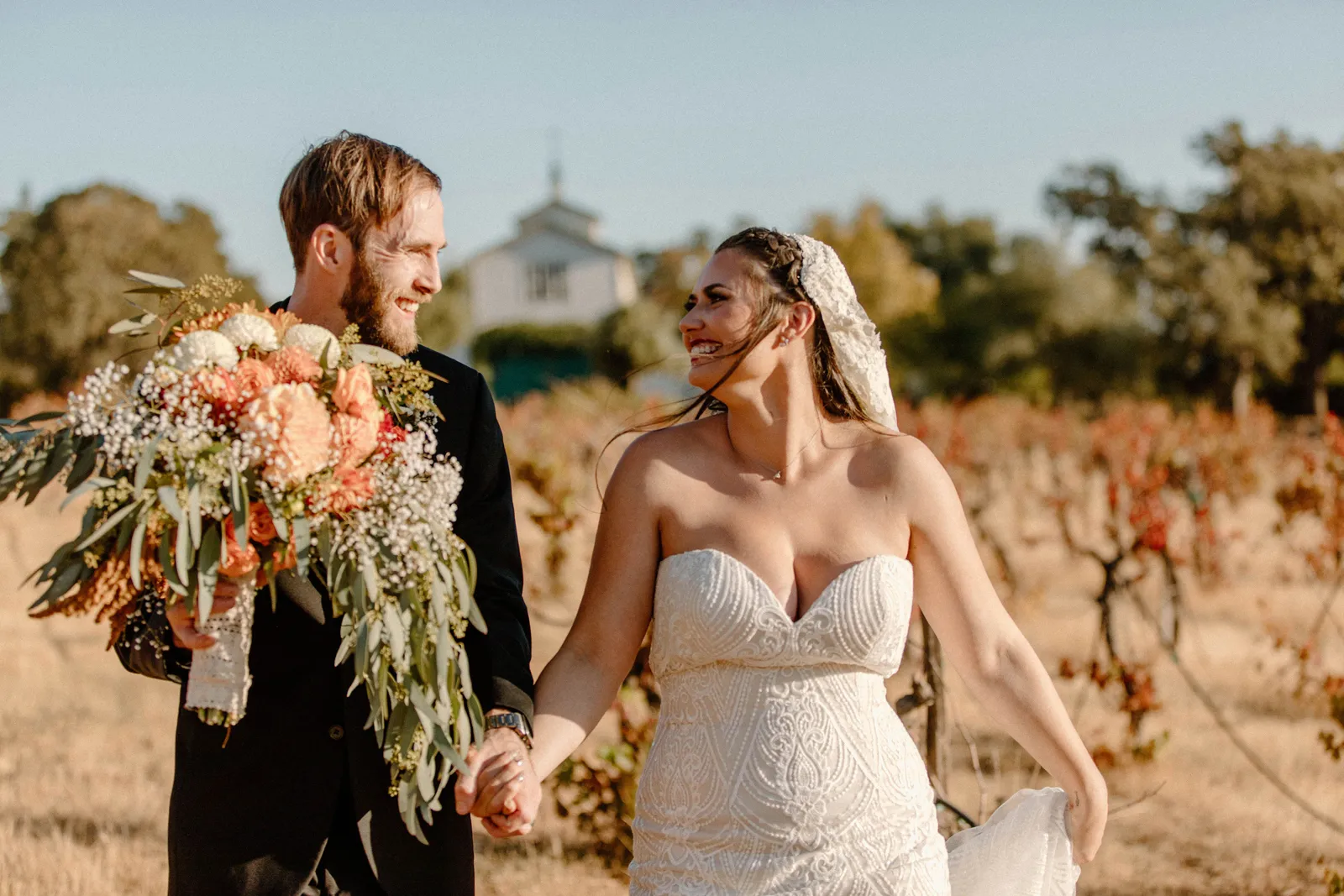 Bride and groom walking through an orchard.