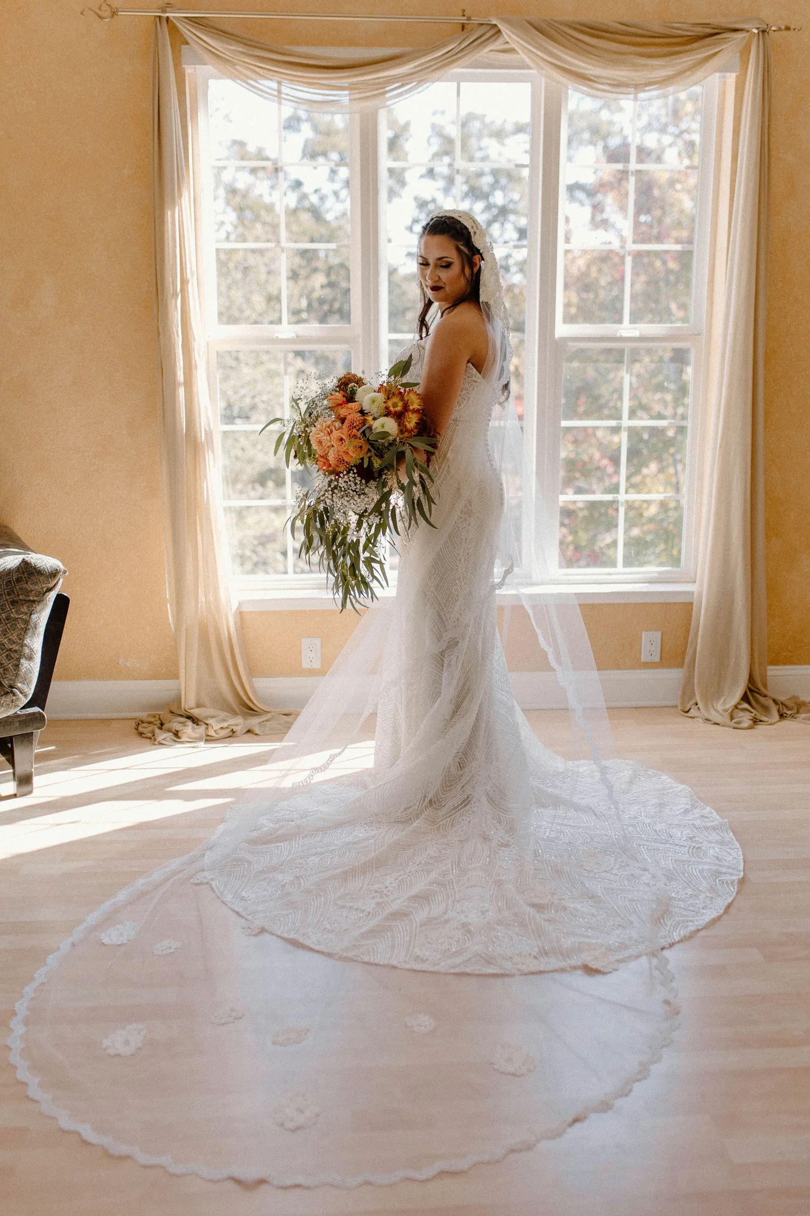 Bride taking photos in her wedding gown with flowers by window