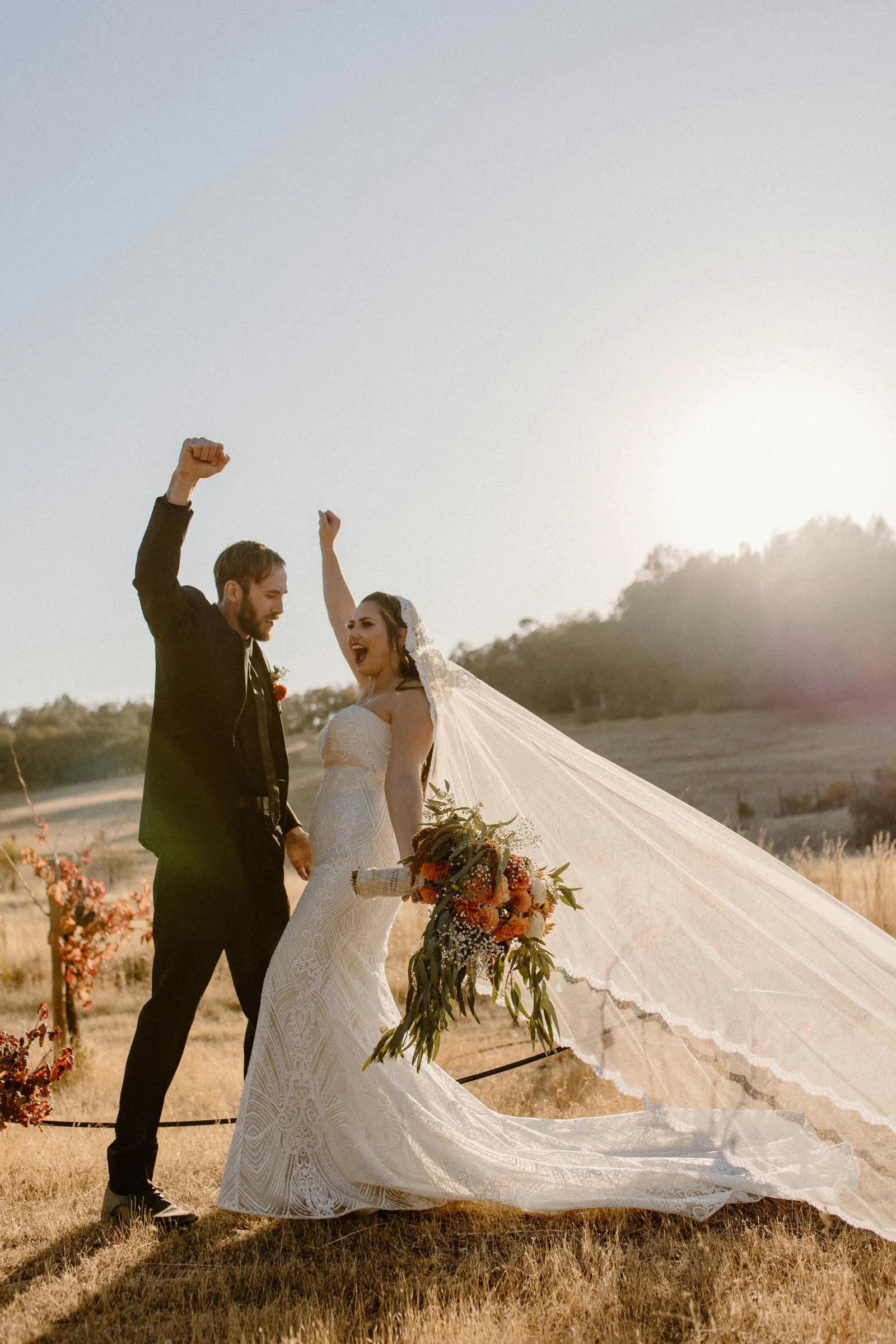 Newlyweds fistpumping in the orchard.