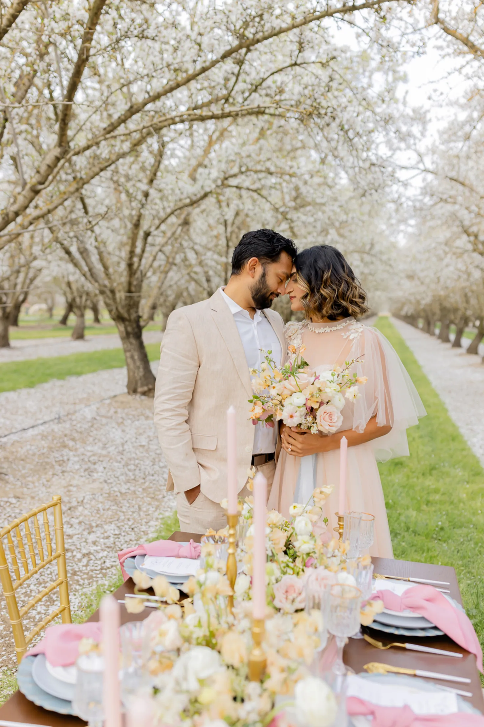 Bride and groom about to kiss at the end of a table in the almond orchard.