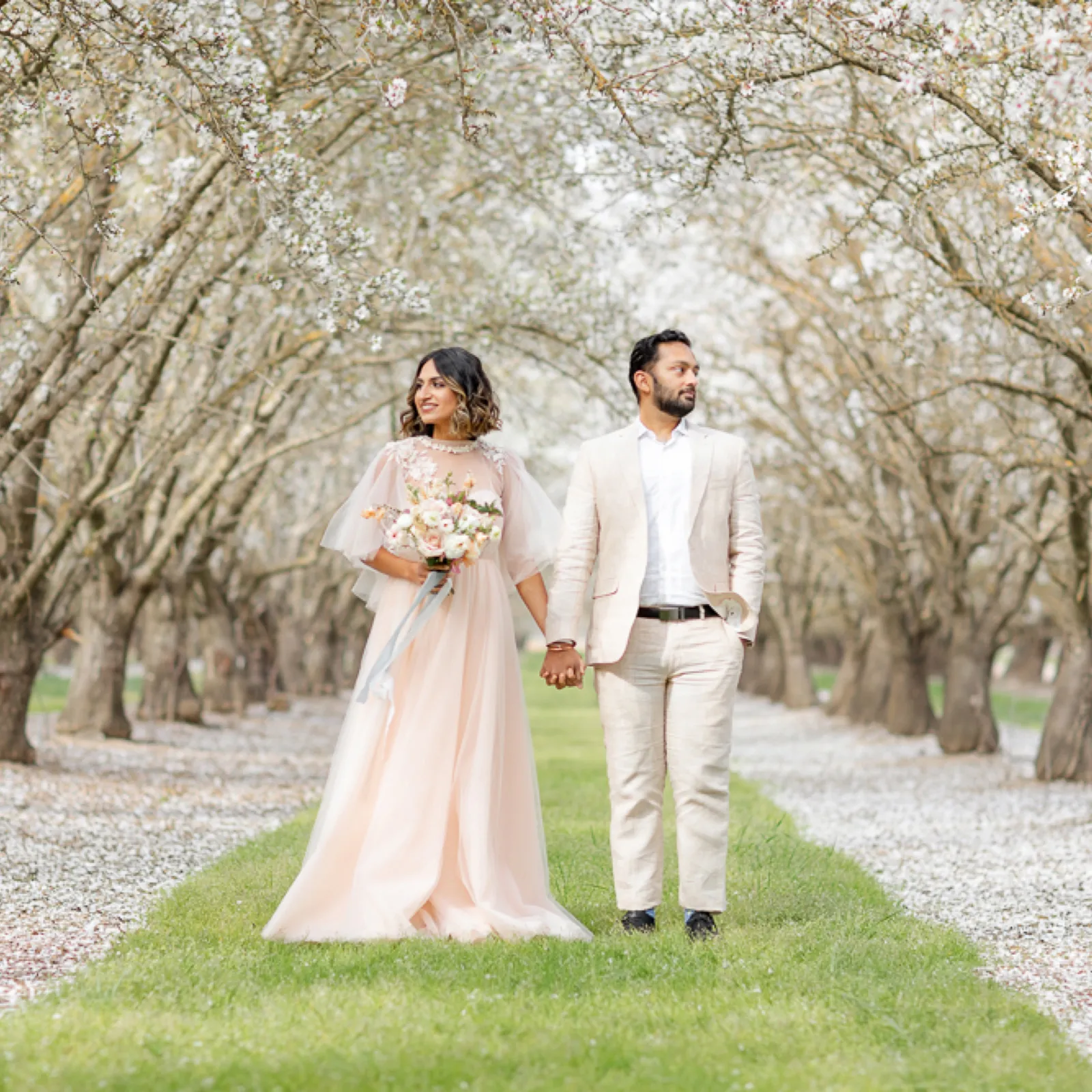 Bride and groom holding hands in the almond orchard.