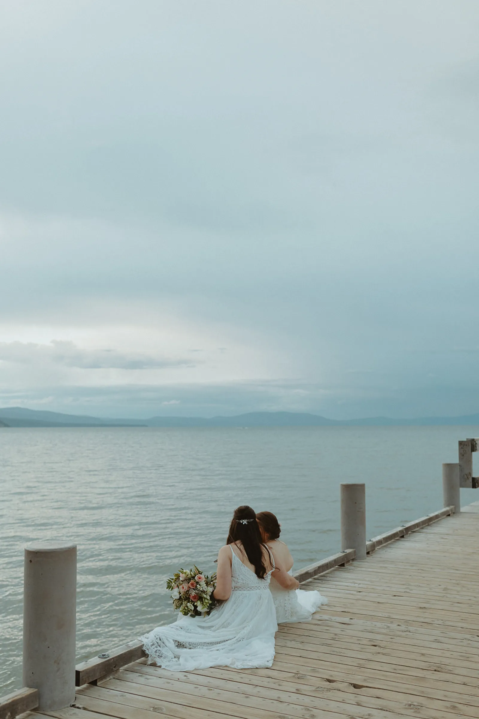 The newlyweds sitting on a dock with their backs to the camera.