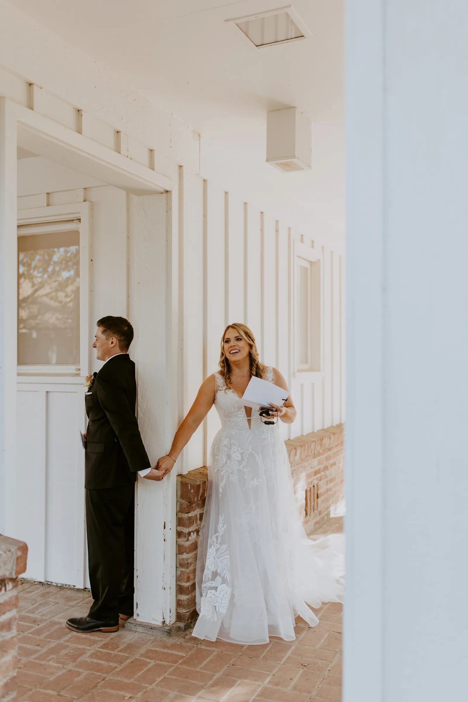 Bride in dress reading vows behind a wall to her husband-to-be