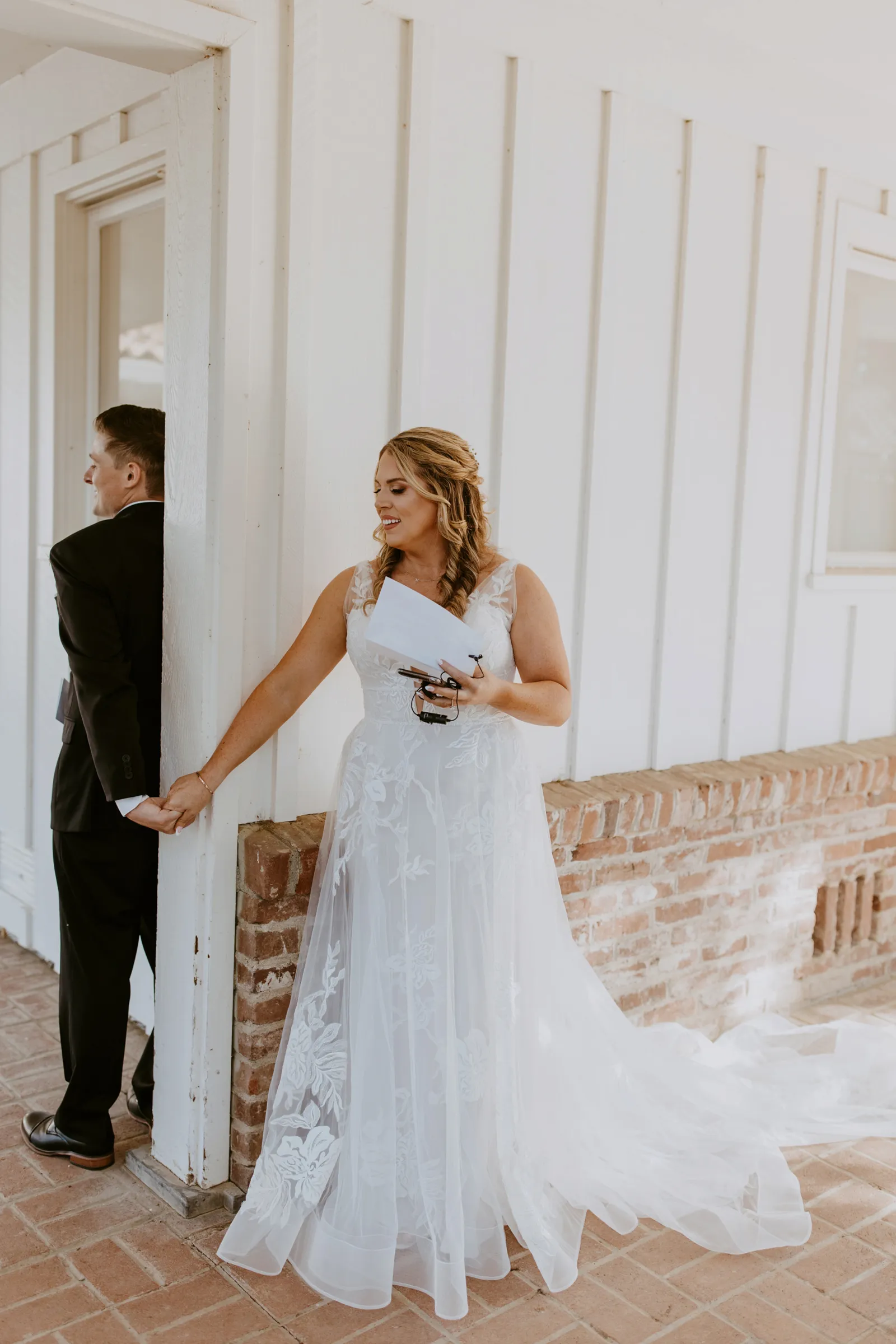 Bride in dress reading vows behind a wall to her husband-to-be