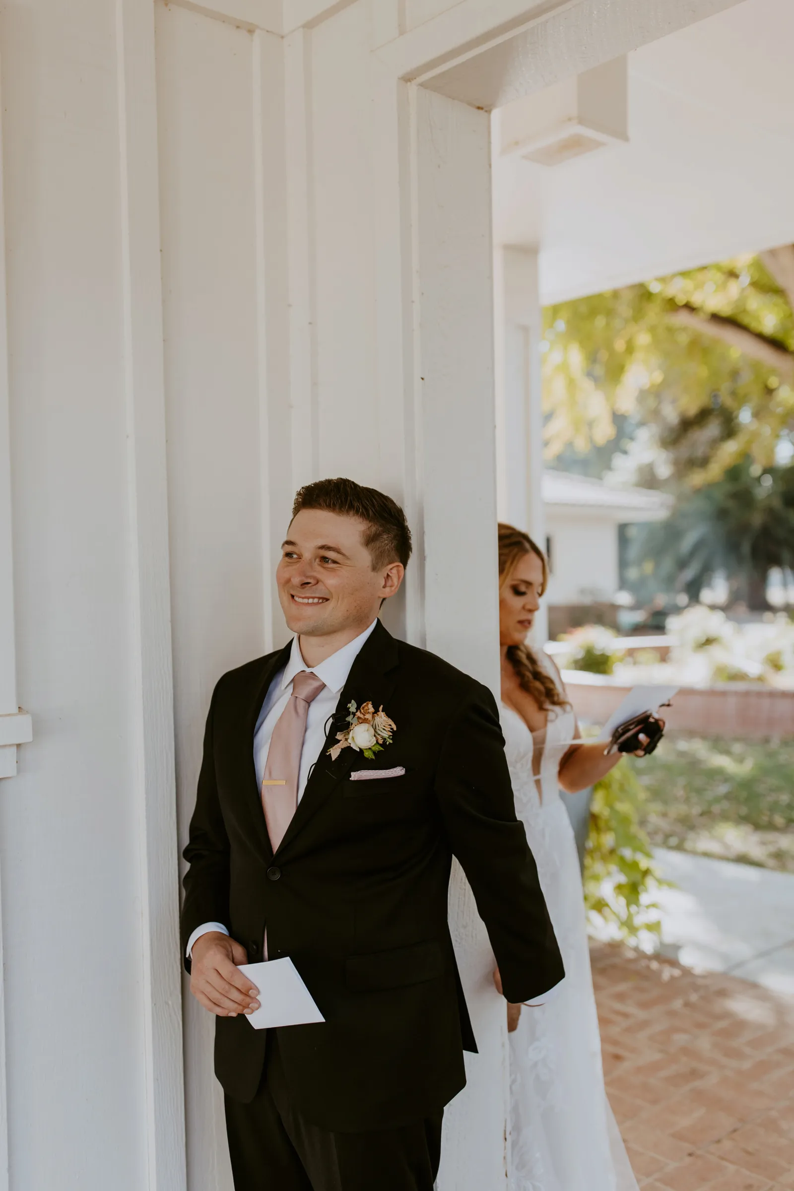 Groom holding his bride-to-be's hand behind a door as she reads her vows