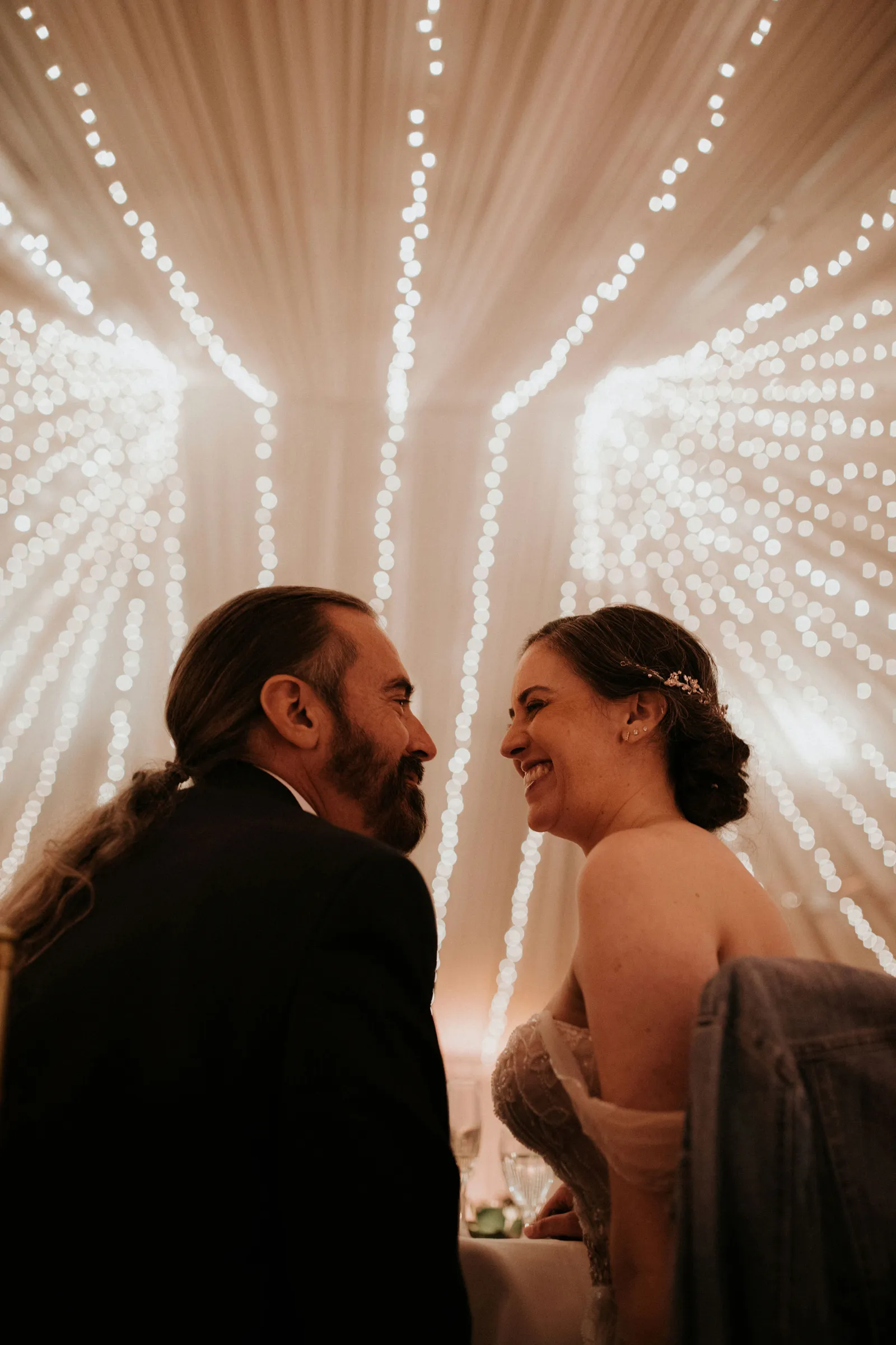 Newlyweds grinning at each other at the reception with their backs to the camera.