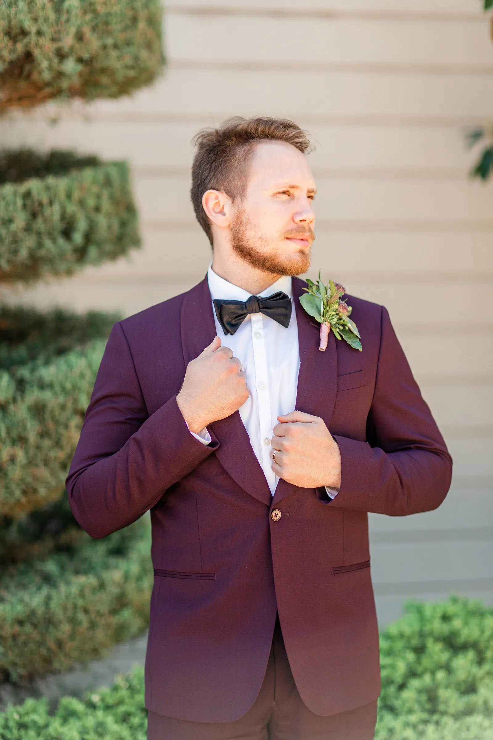 Groom in a maroon suit posing.