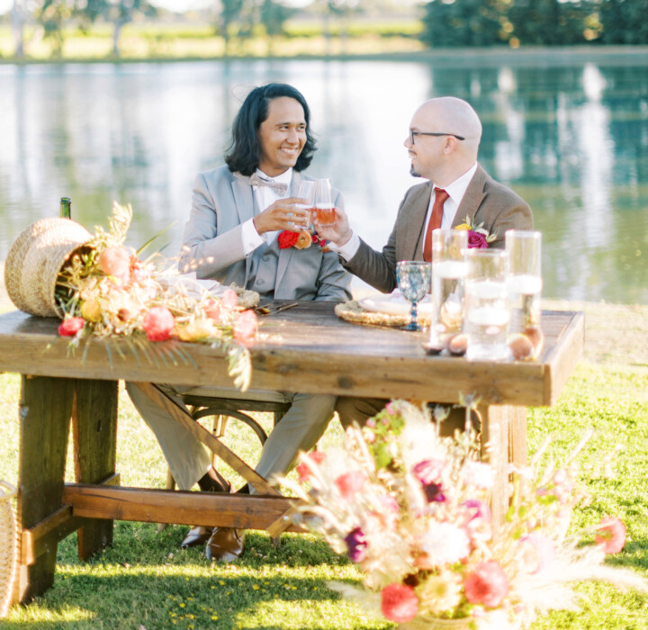 Grooms cheersing in front of a lake