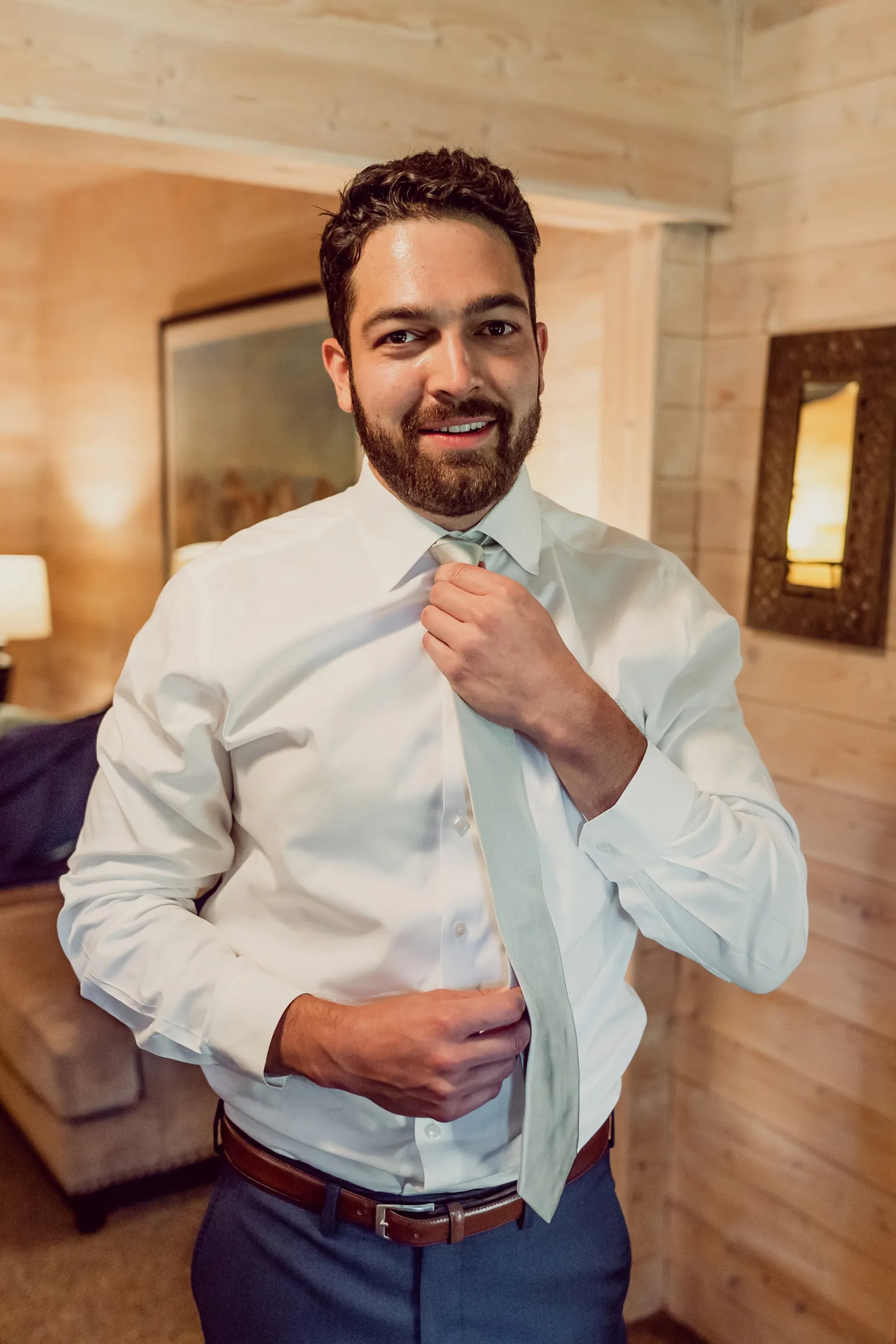 Groom fixing his tie and looking into the camera.