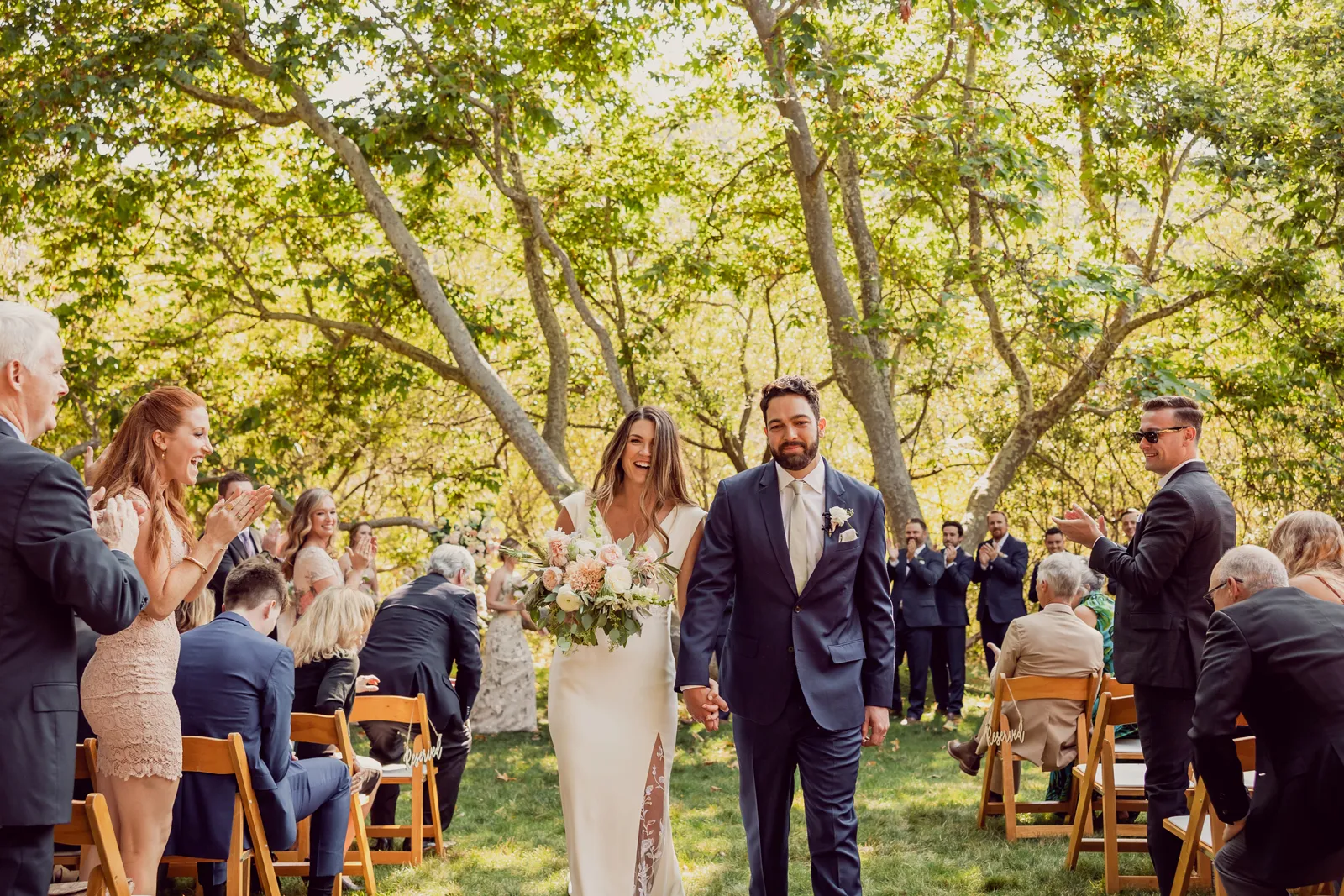 Newlyweds holding hands and walking down the aisle while smiling.