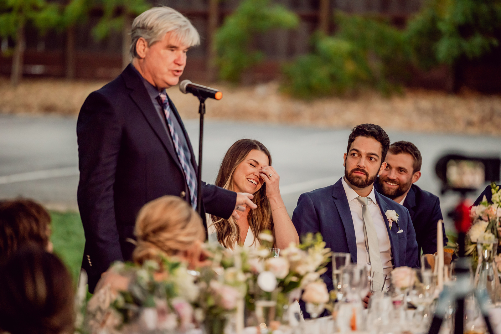 Father of the bride giving a speech while she laughs.