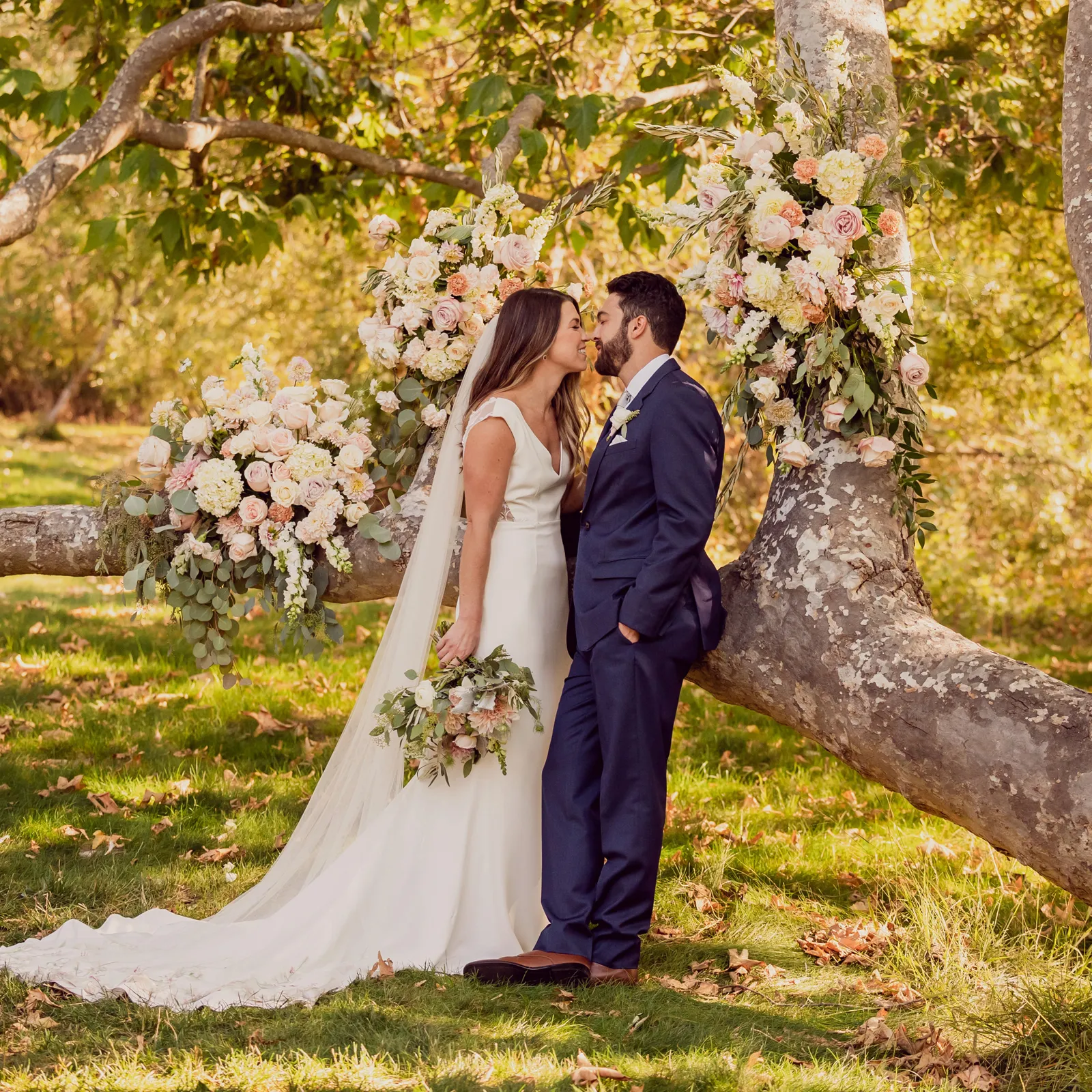 Bride and groom about to kiss as groom leans against a tree.