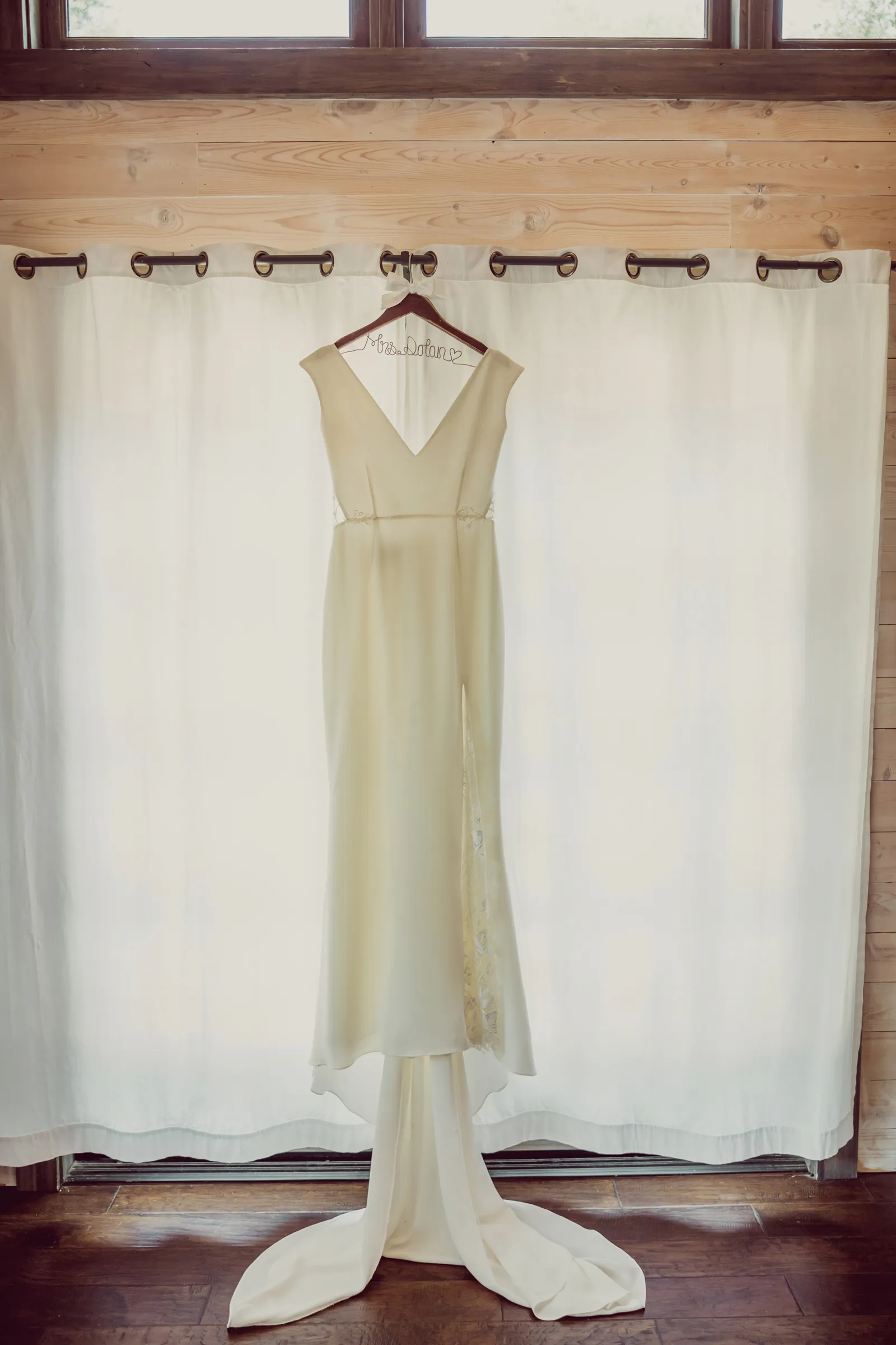 Wedding gown hanging on a hook, in front of a closed window.