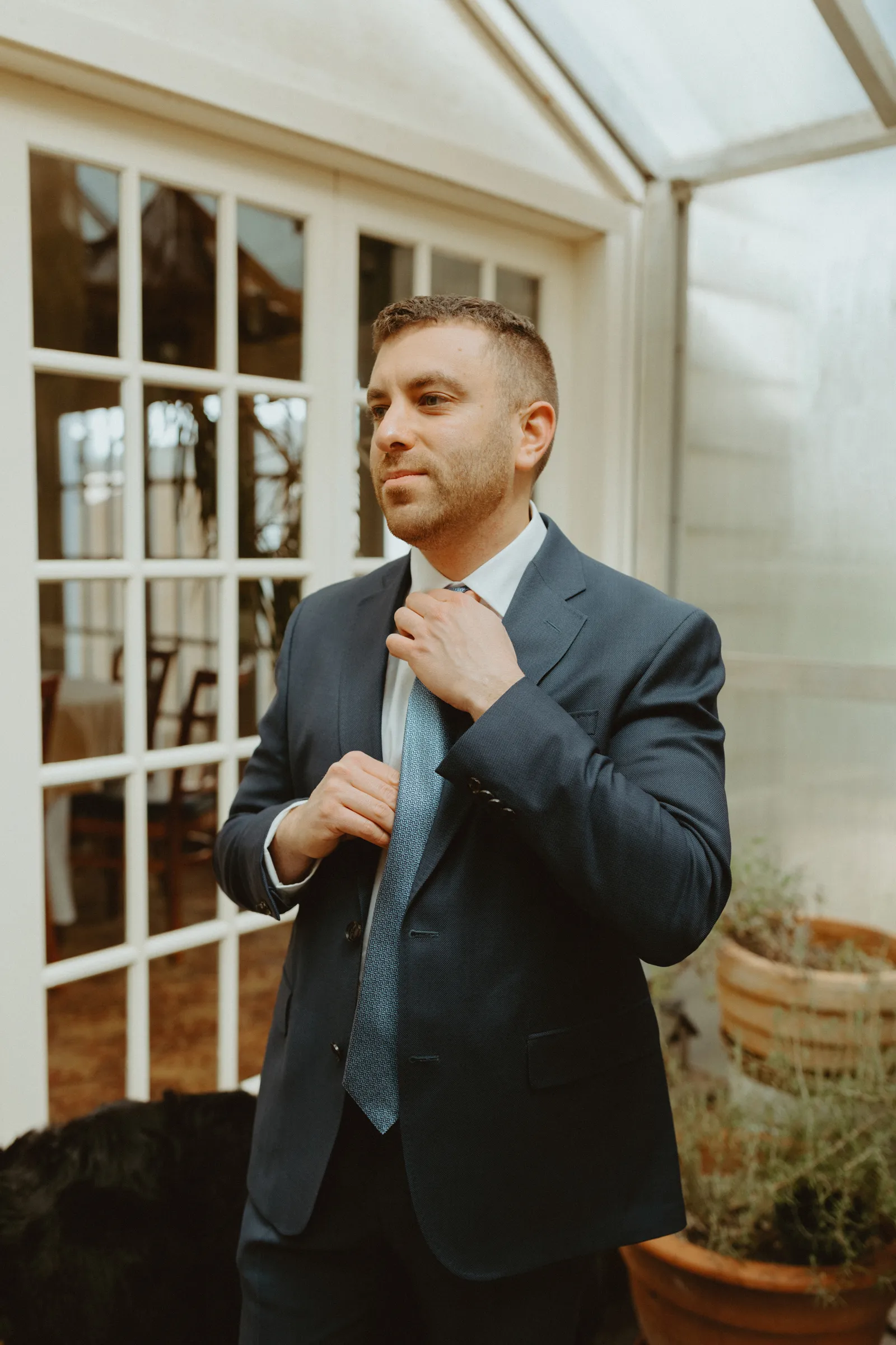 Groom fixing his tie and looking into the distance.