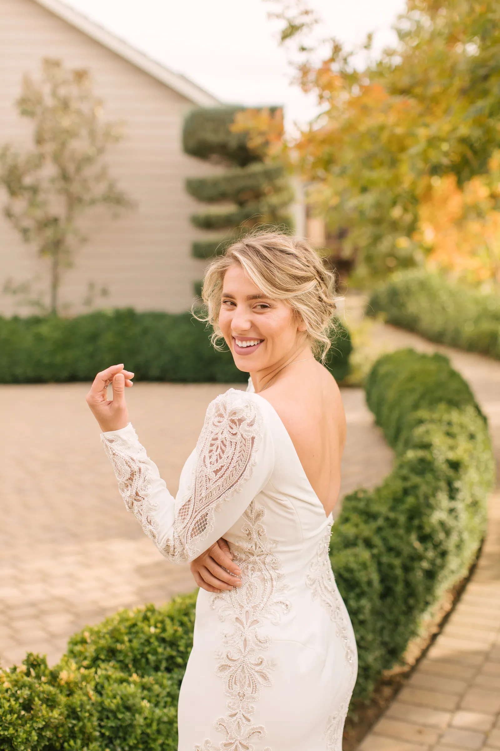 Bride wearing open back gown, and smiling over her shoulder at the camera.