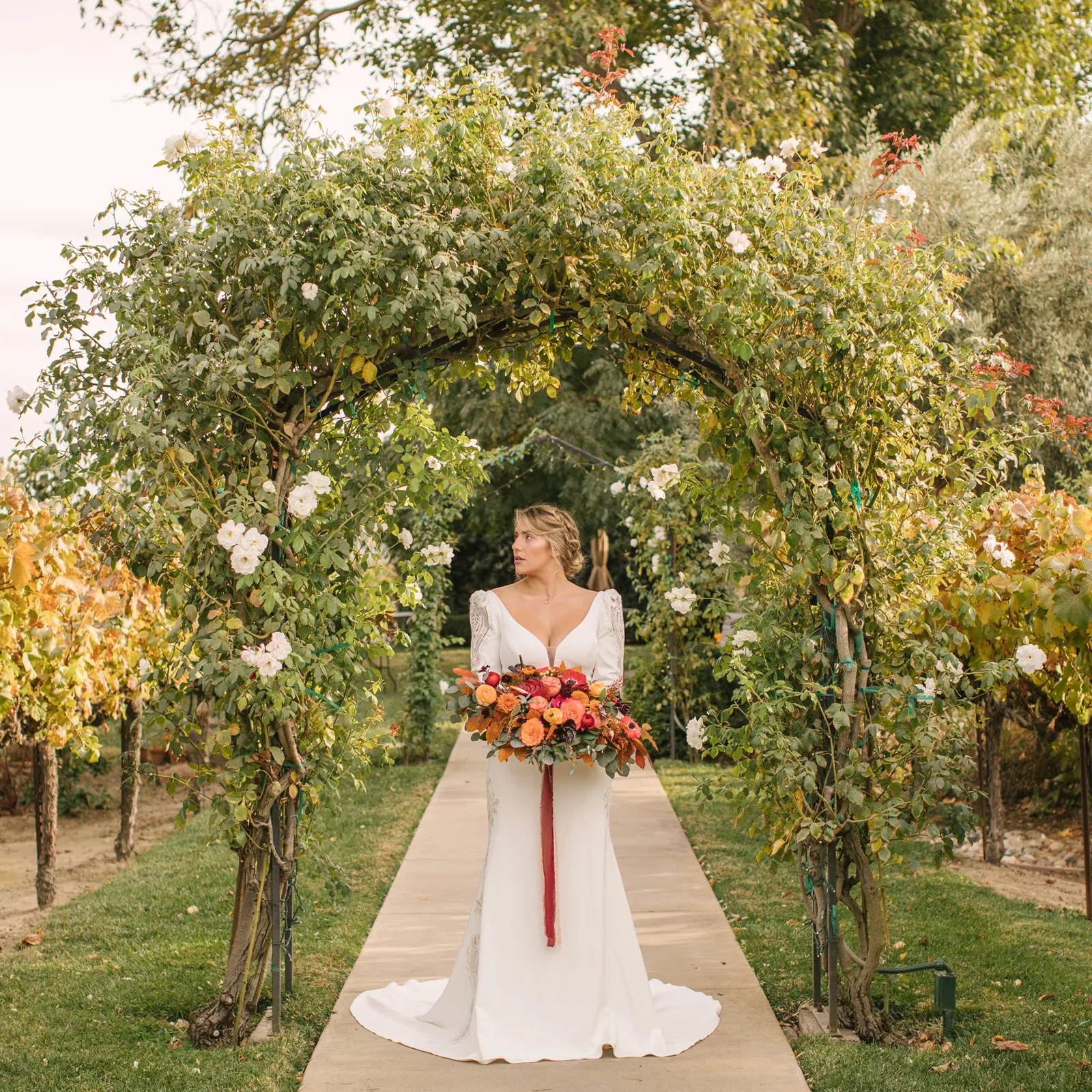 Bride holding flowers underneath a green, rustic, arch.