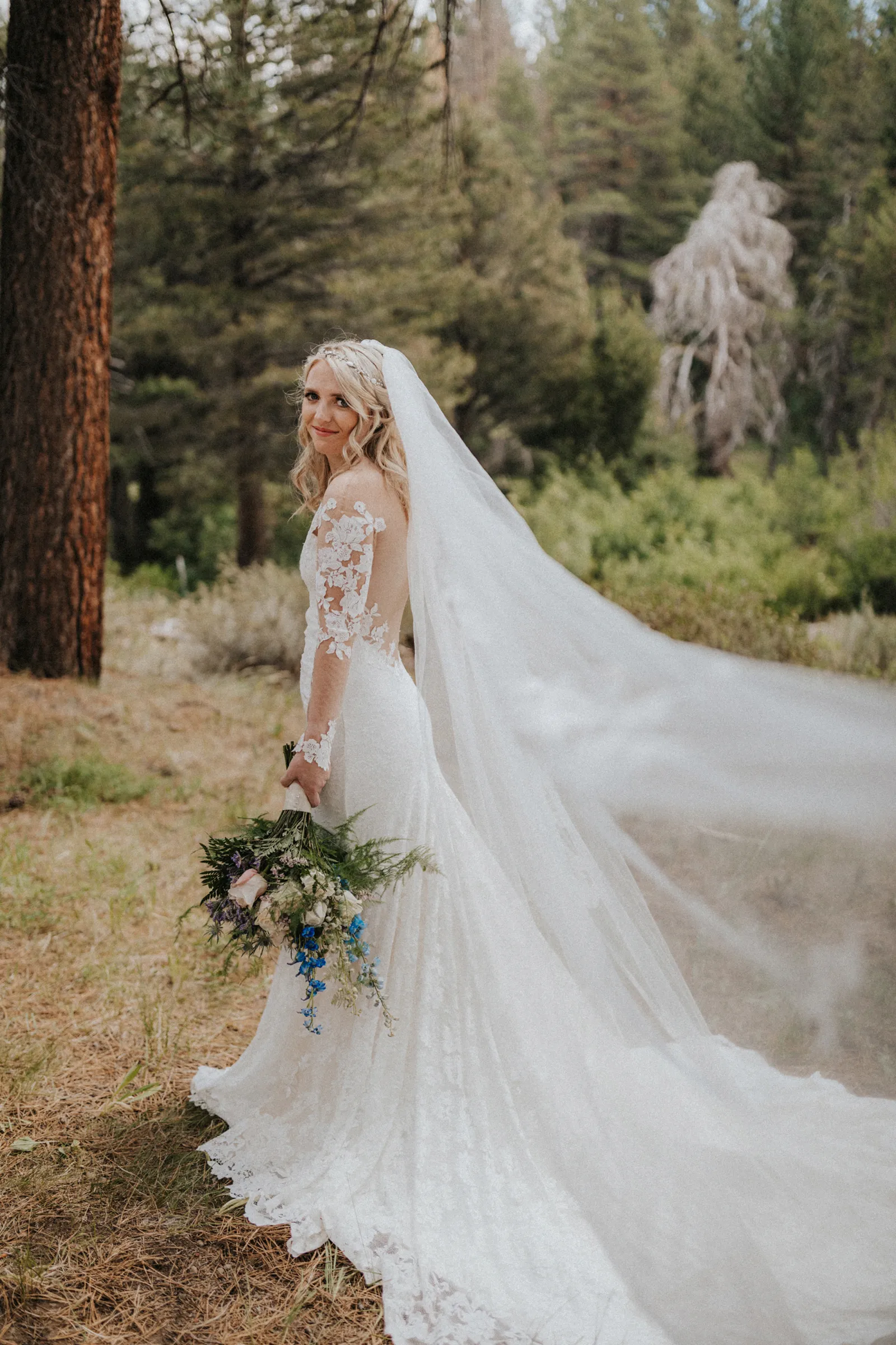 Bride standing in the woods with her bouquet, looking back at the camera.