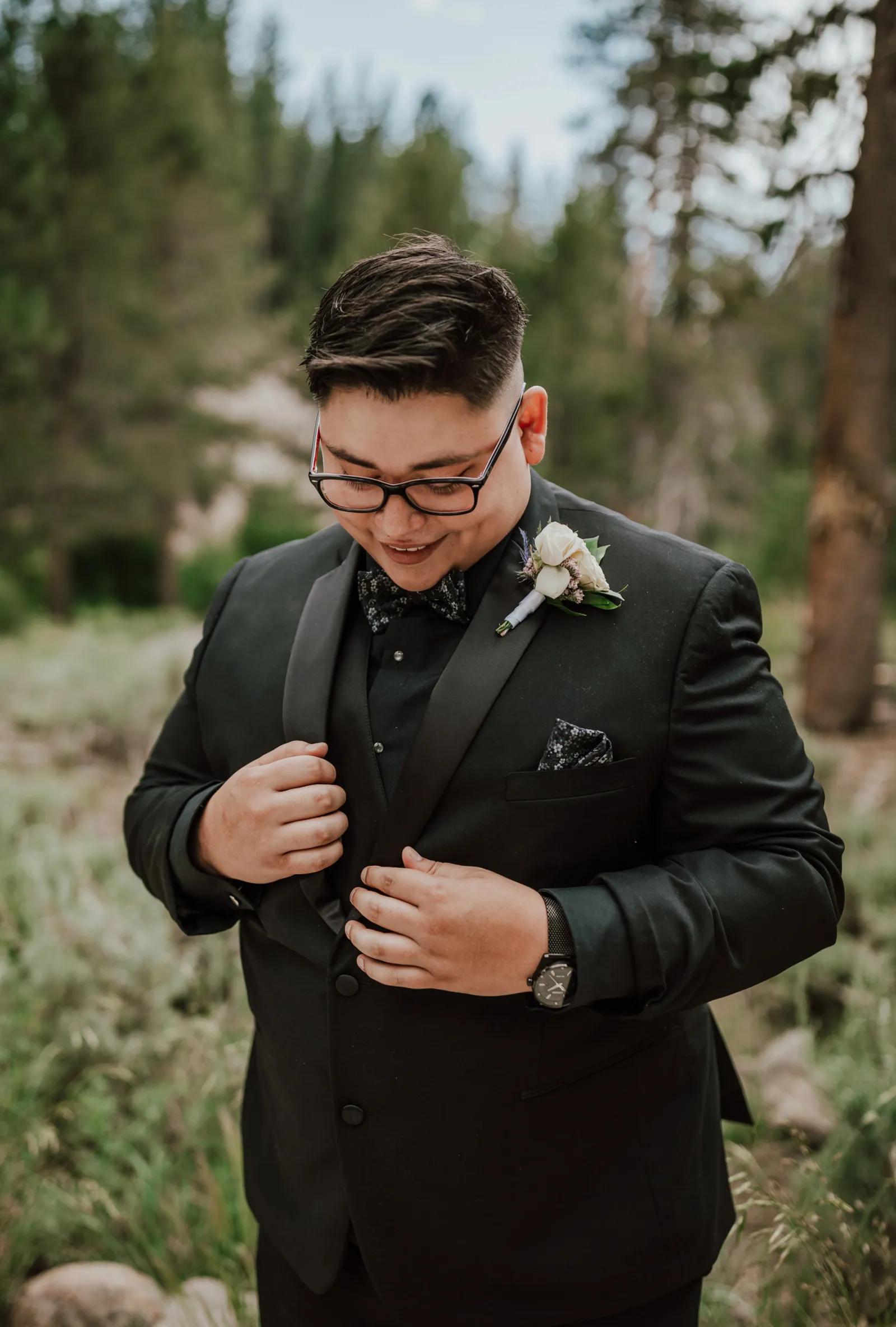 Groom fixing his tuxedo lapel and smiling.