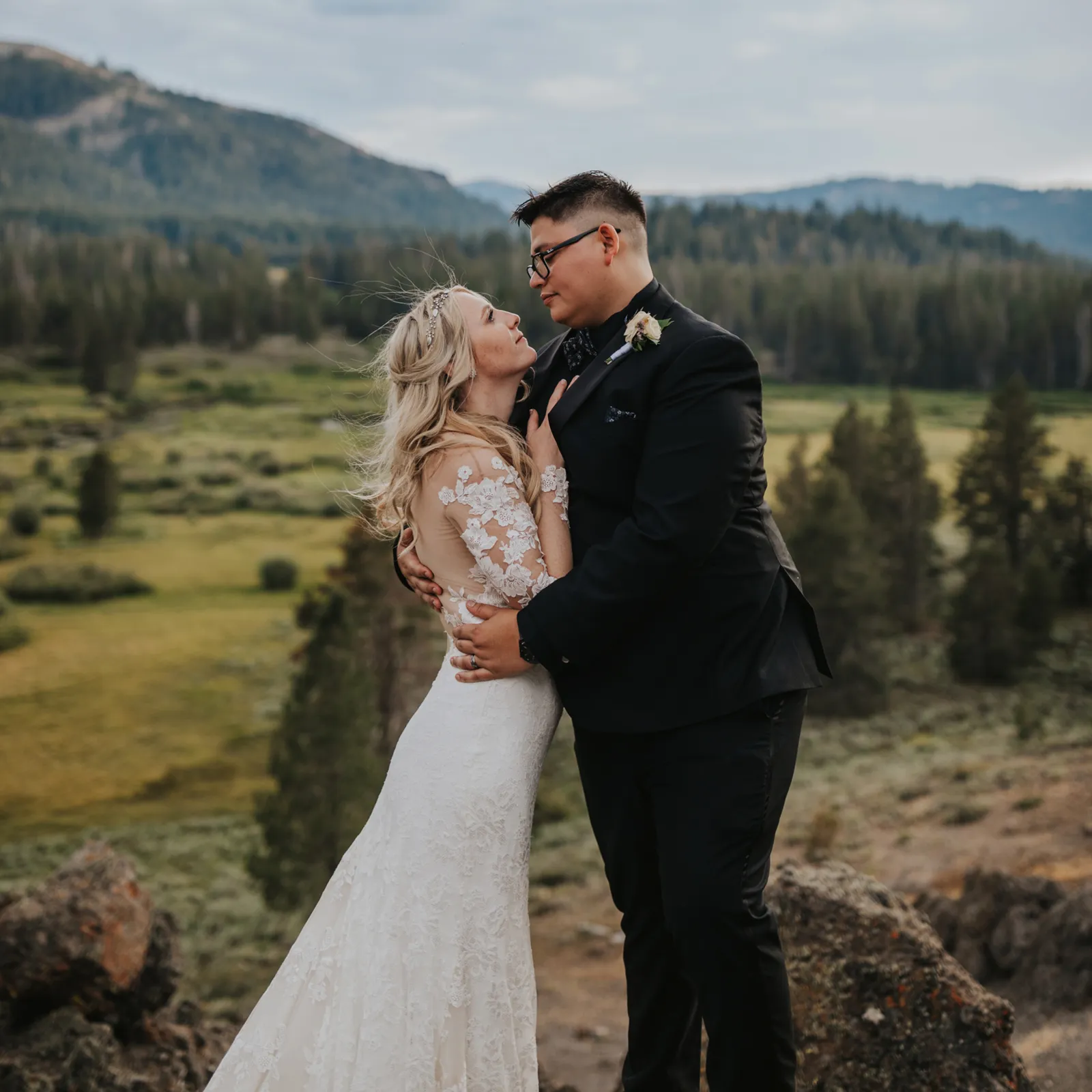 Bride and groom looking into each other's eyes on a hill overlooking the forest.