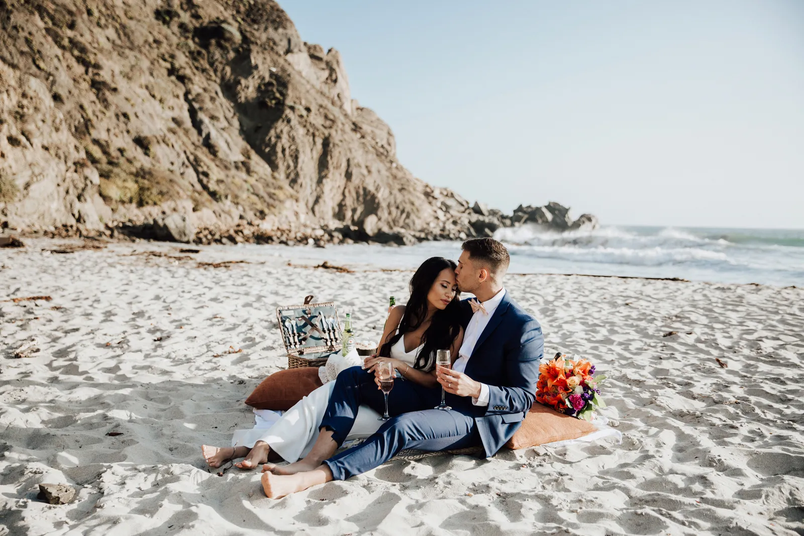 Groom kissing his bride on the forehead during their beach picnic.