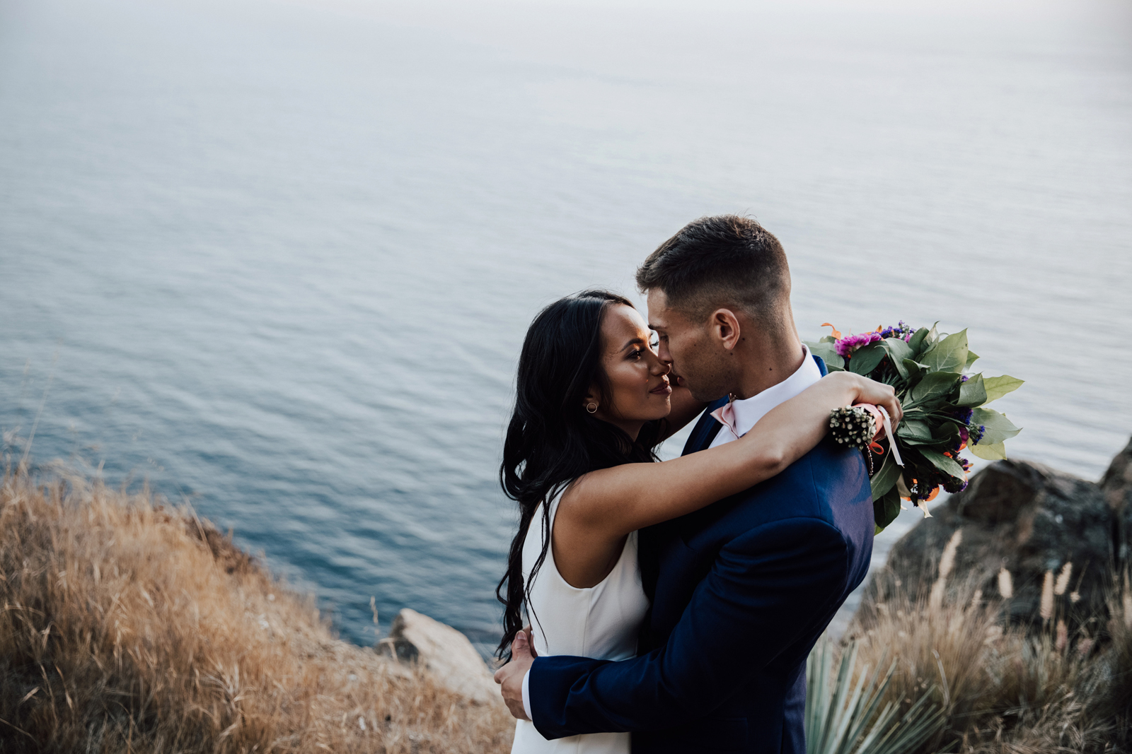 Bride and groom kissing overlooking the ocean.