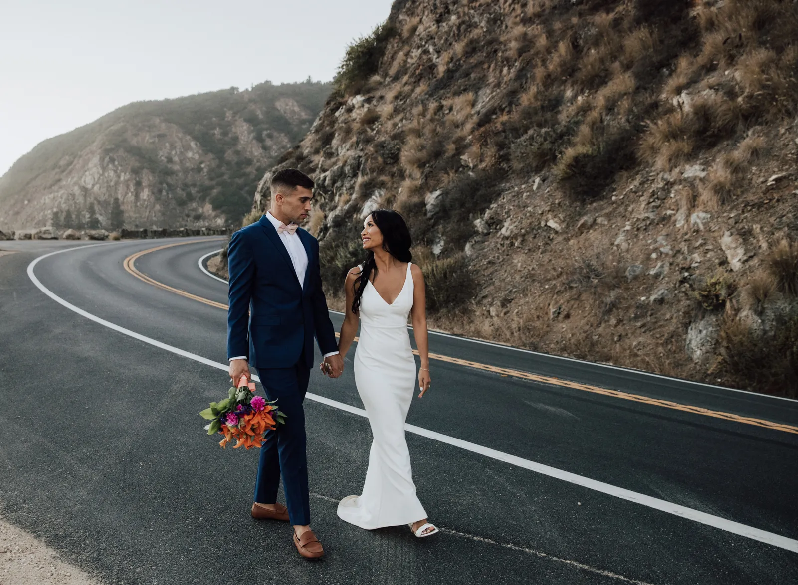 Bride and groom holding hands and walking down a road.