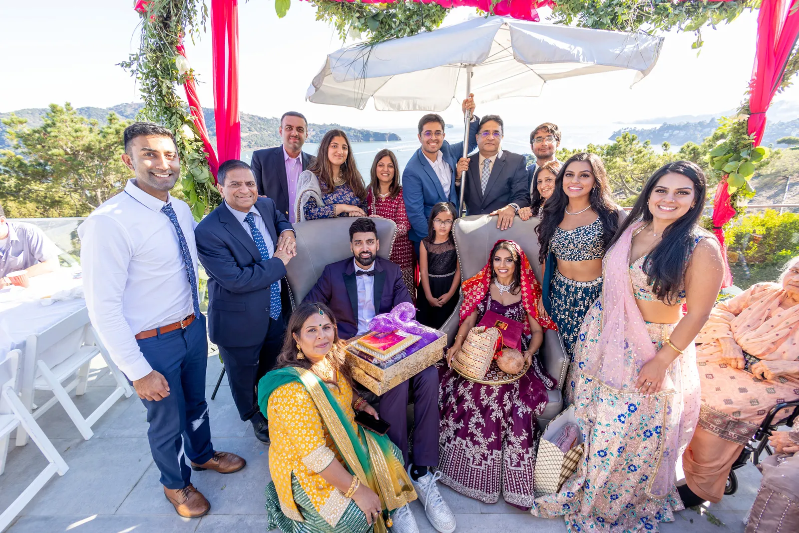 Bride and groom in traditional Indian wedding attire smiling with their family.