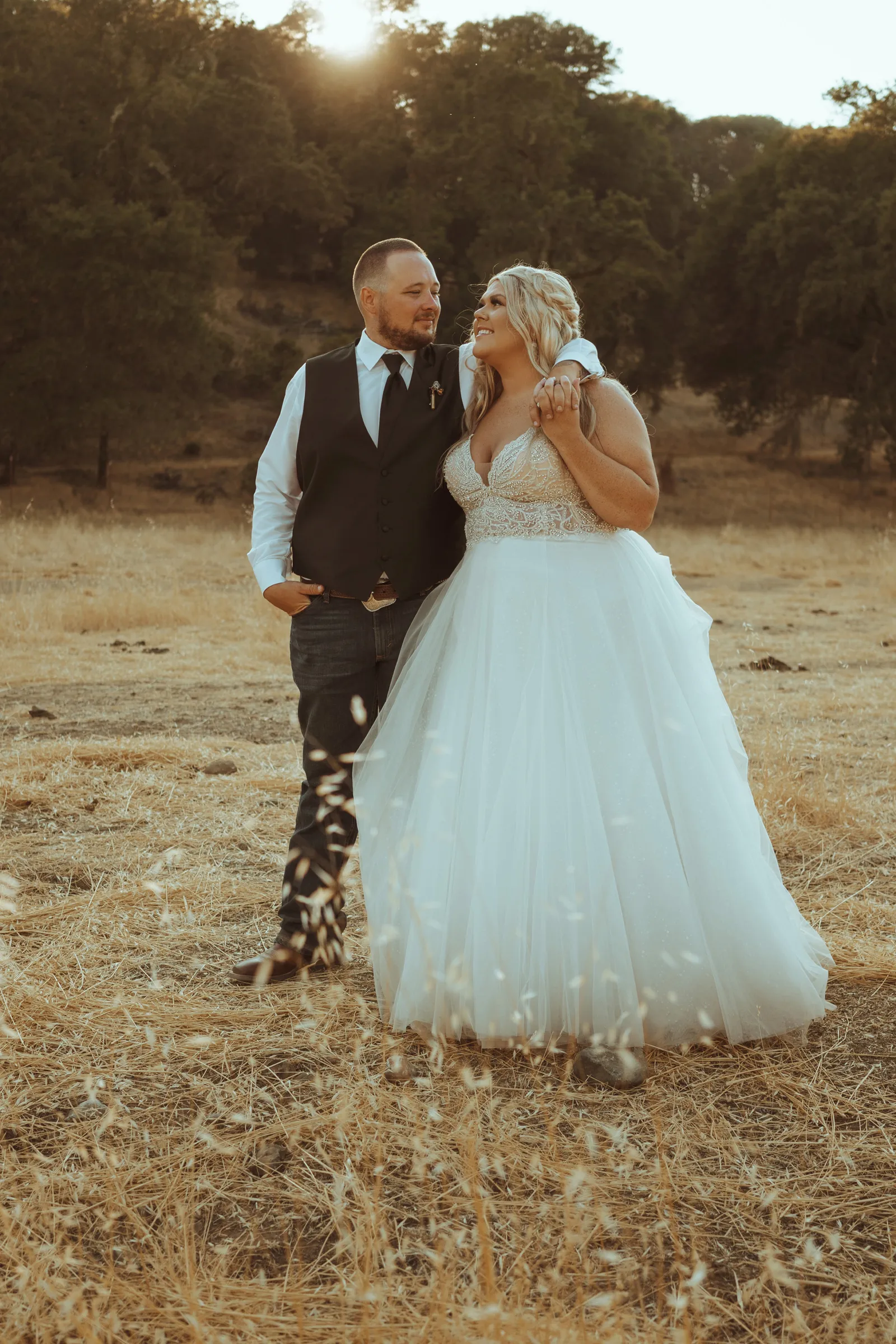 Bride and groom smiling at each other in a field.