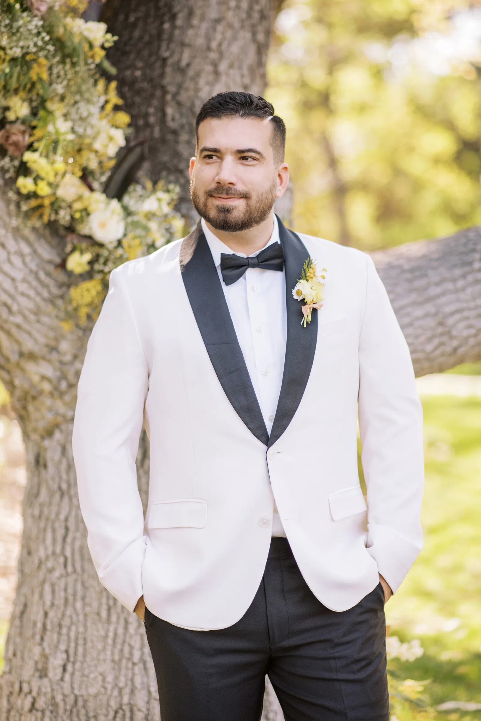 Groom in a white tux smiling with his hands in his pockets.