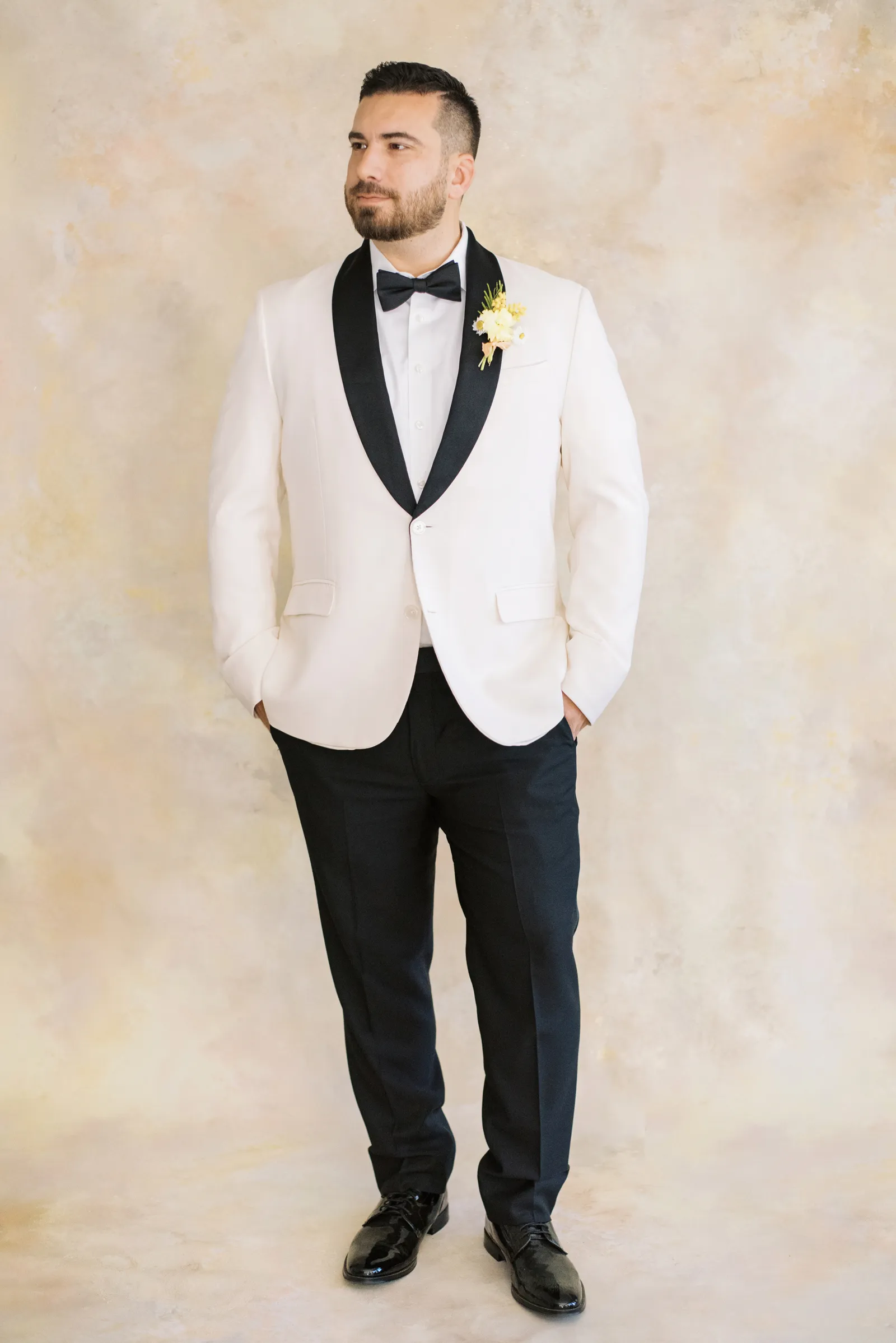 Groom with hands in his pockets in with a pale backdrop.