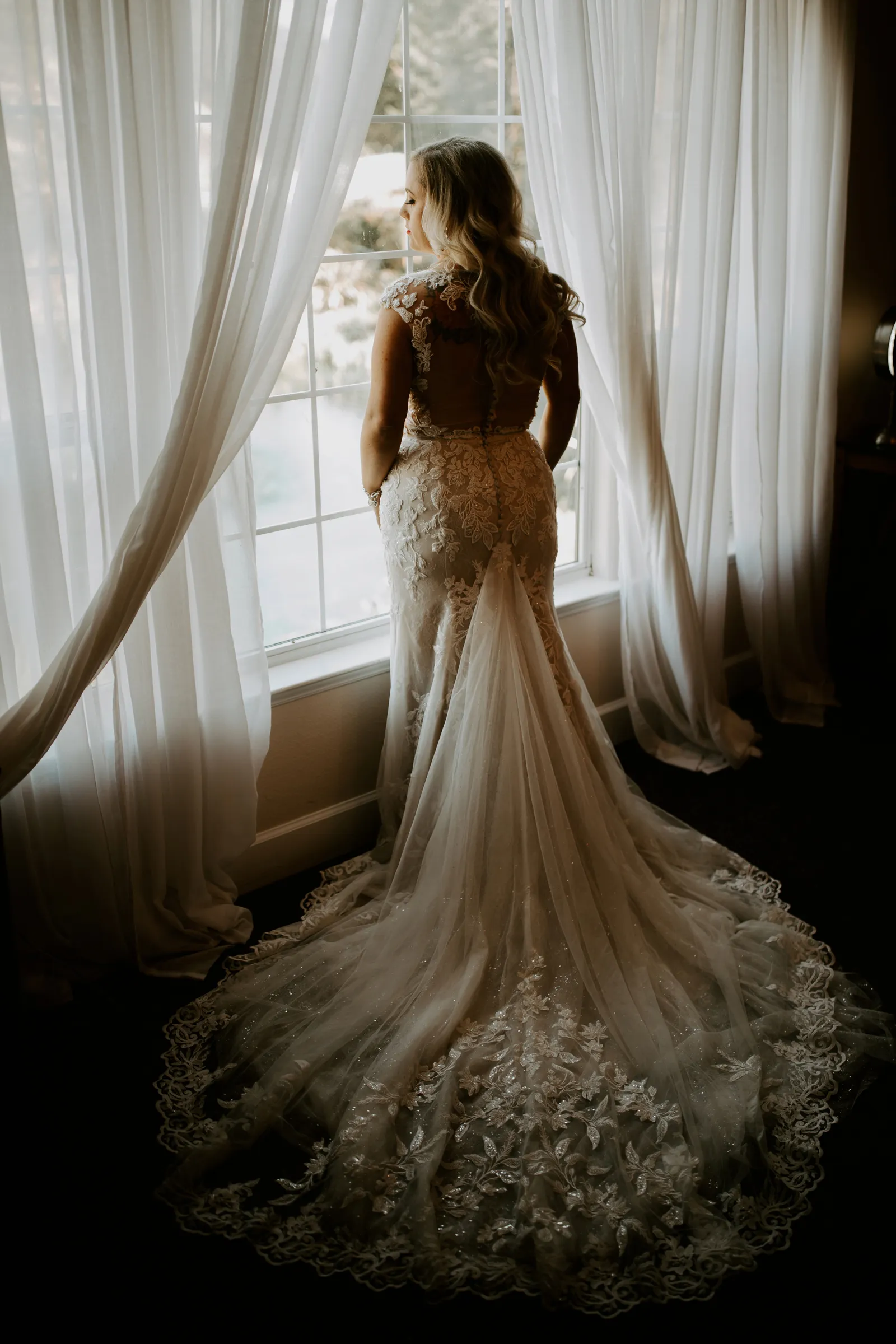 Bride looking out of the curtains with her back to us.