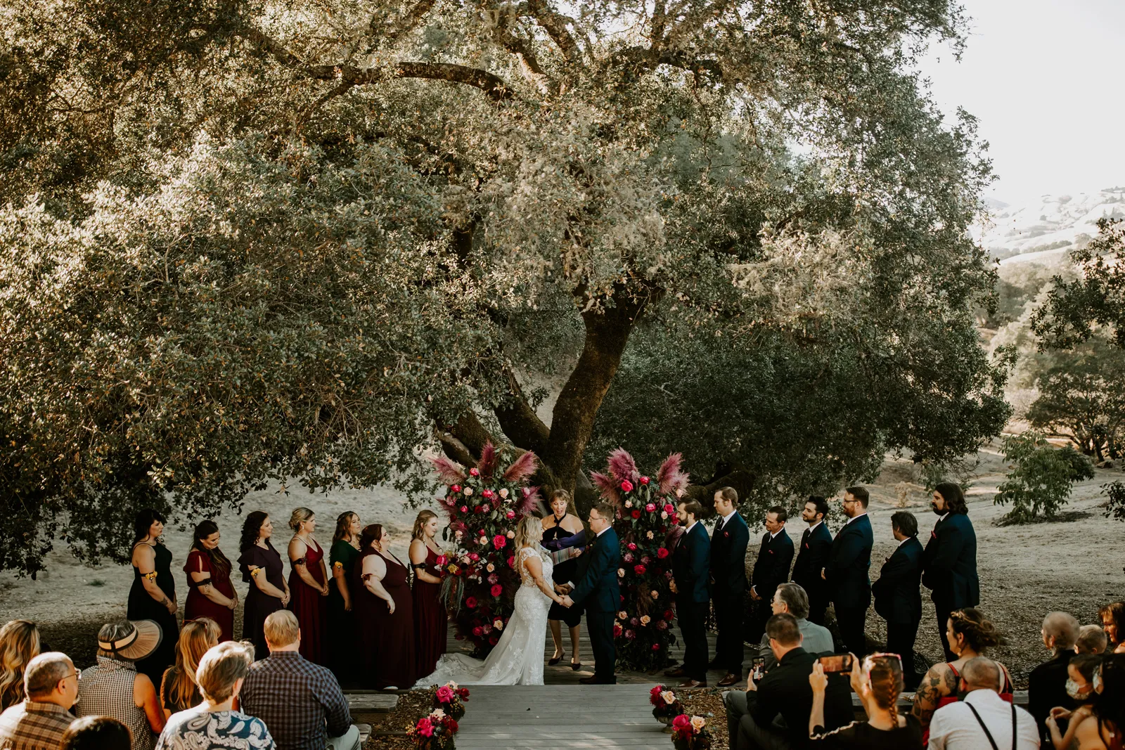 Bride and groom holding hands near the flower arch as their guests sit and watch.