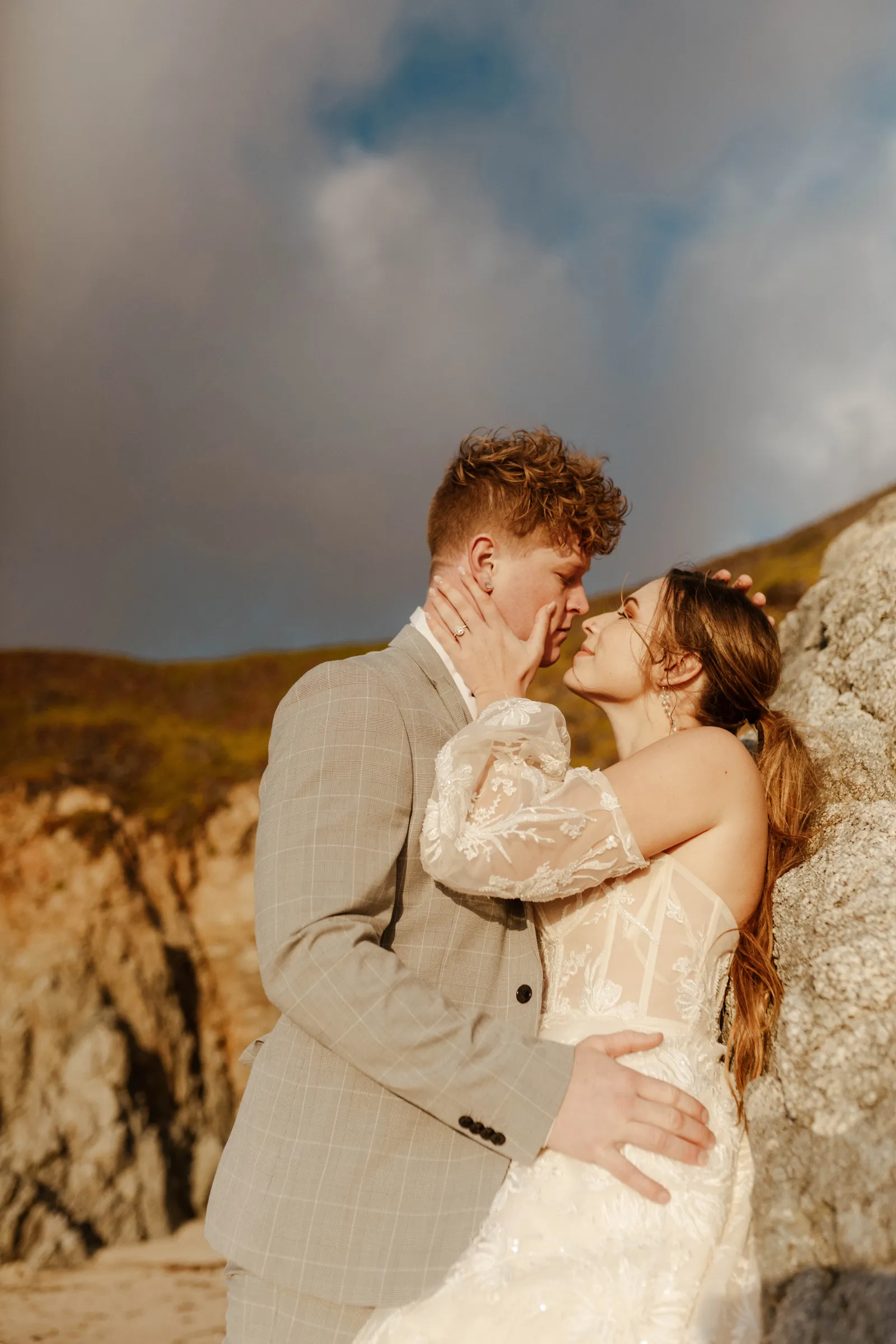 Bride holding her husband's cheek against a cliffside.