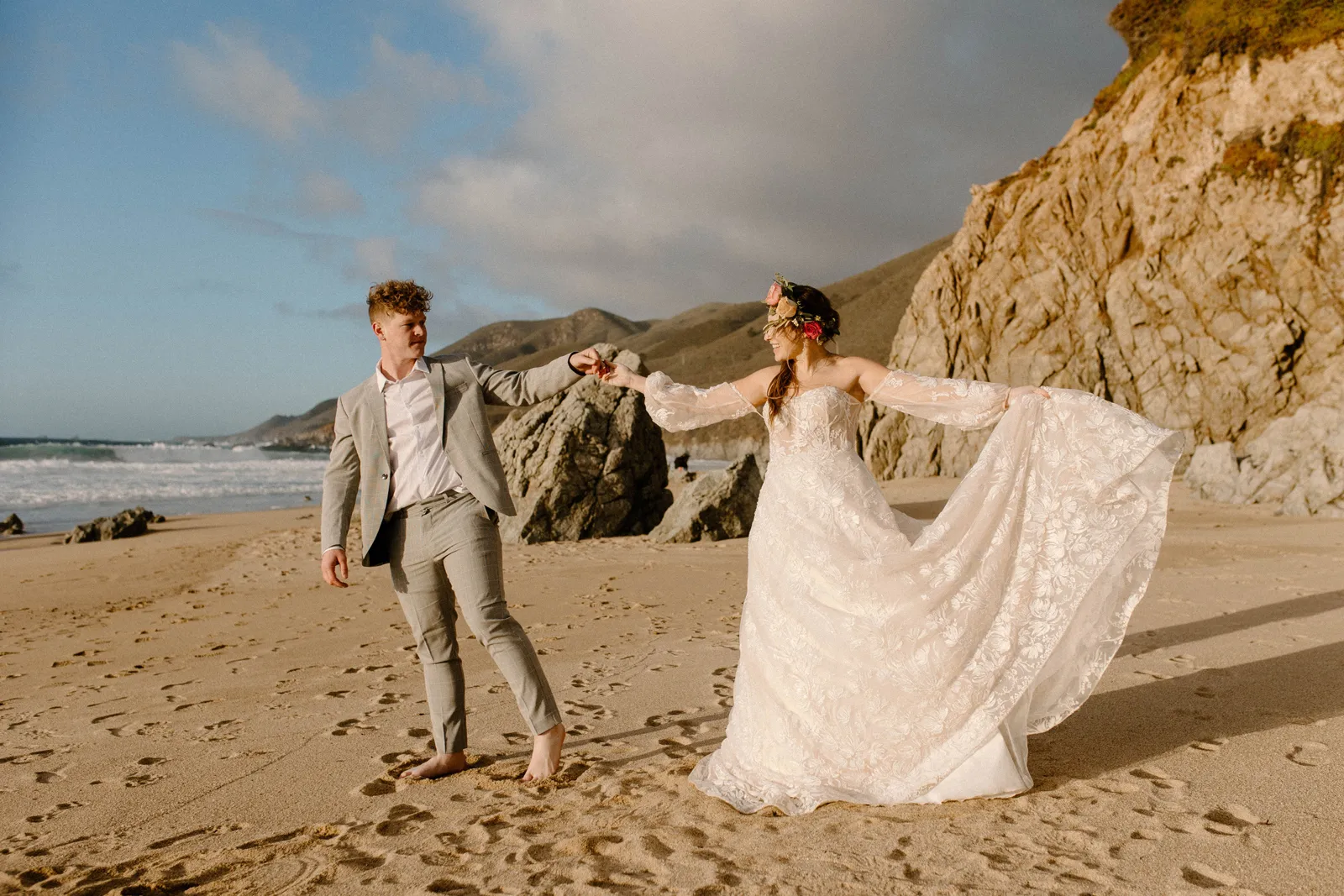 Groom and Bride holding hands as she holds out her dress on the beach.