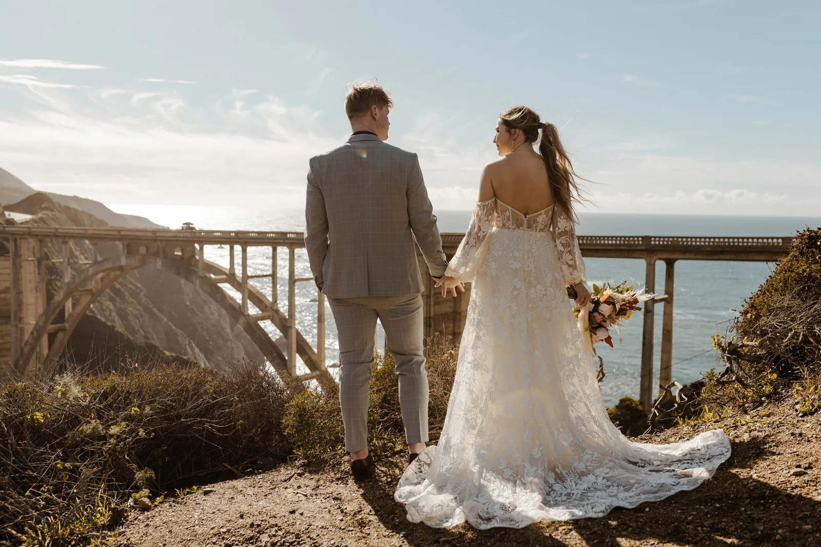 Bride and groom holding hands and looking at the Monterey bridge.