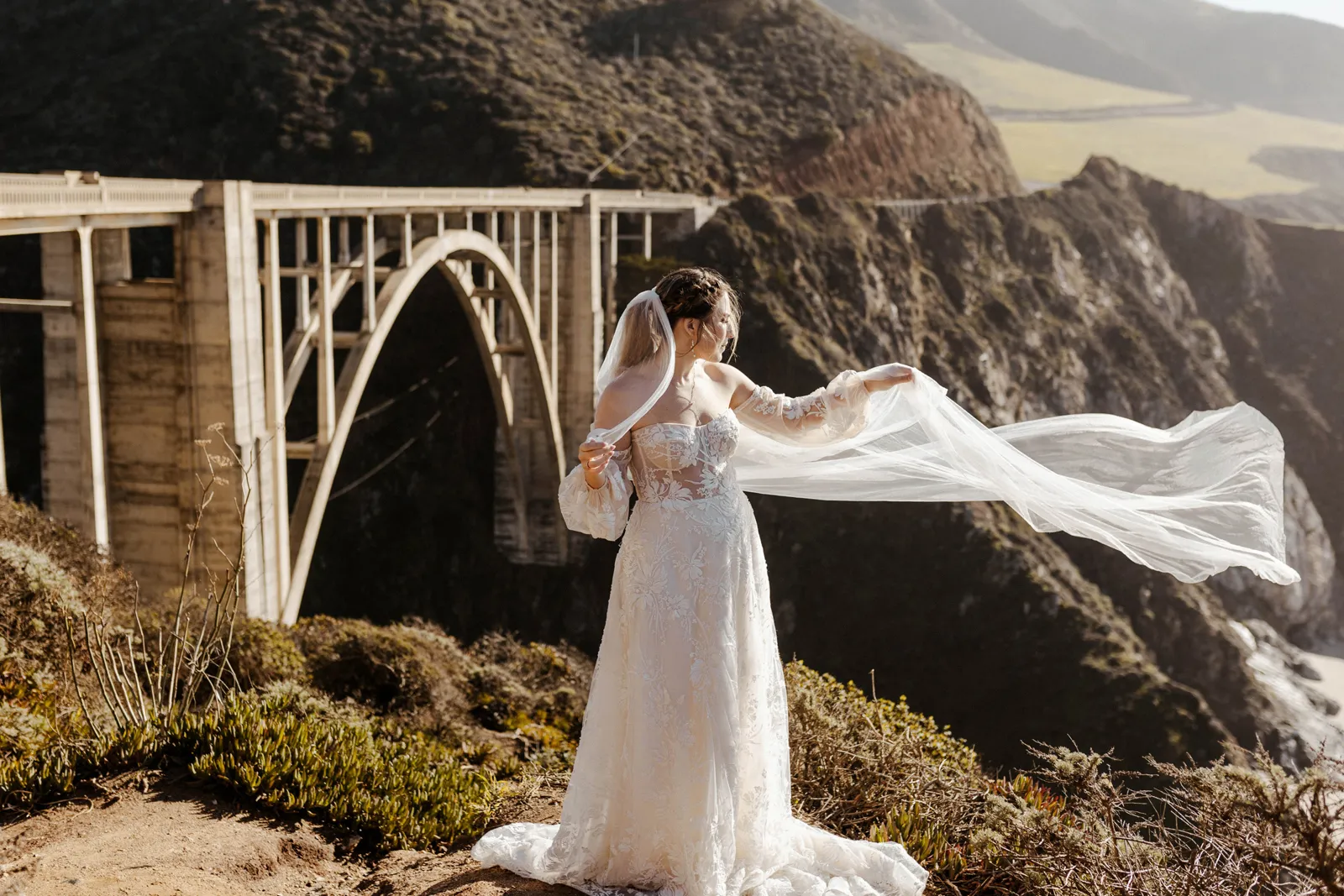 Full body photo of a bride holding her veil near the Monterey Bridge.