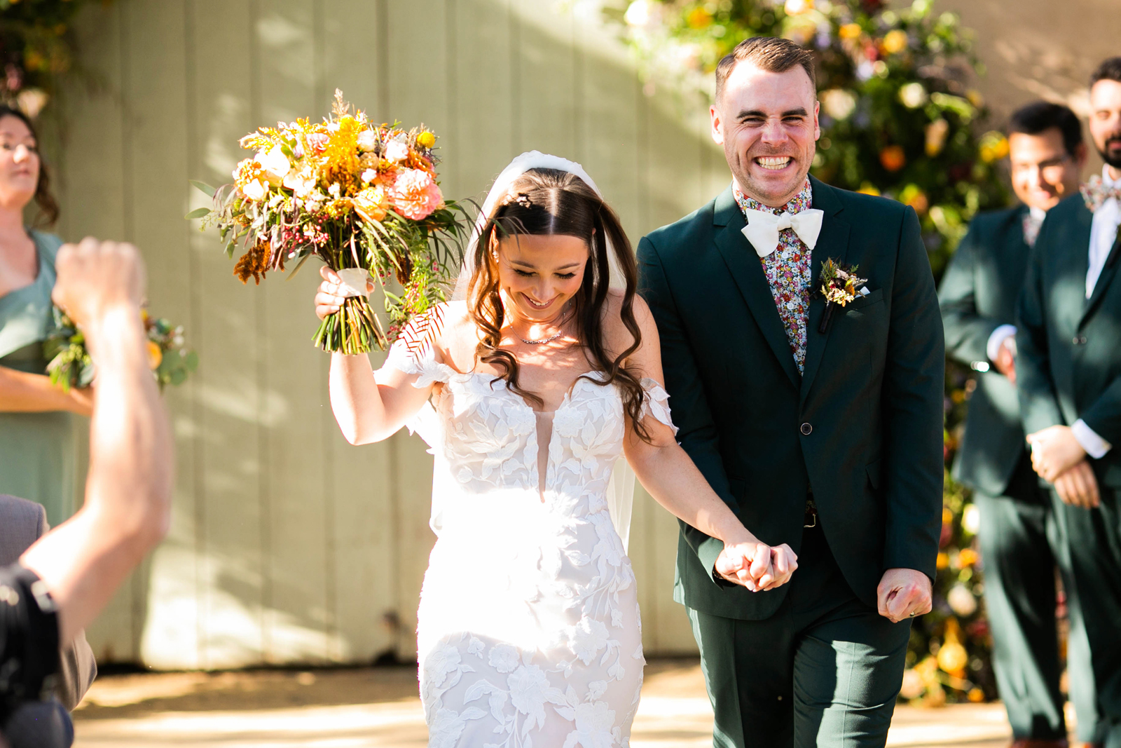 Bride and groom smiling as they walk down the aisle together while everyone claps.