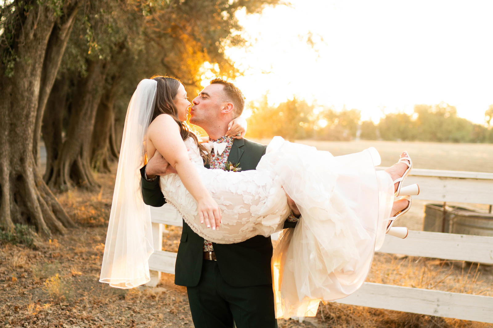 Groom holding his wife, "bridal style" and kissing her as the sun sets.