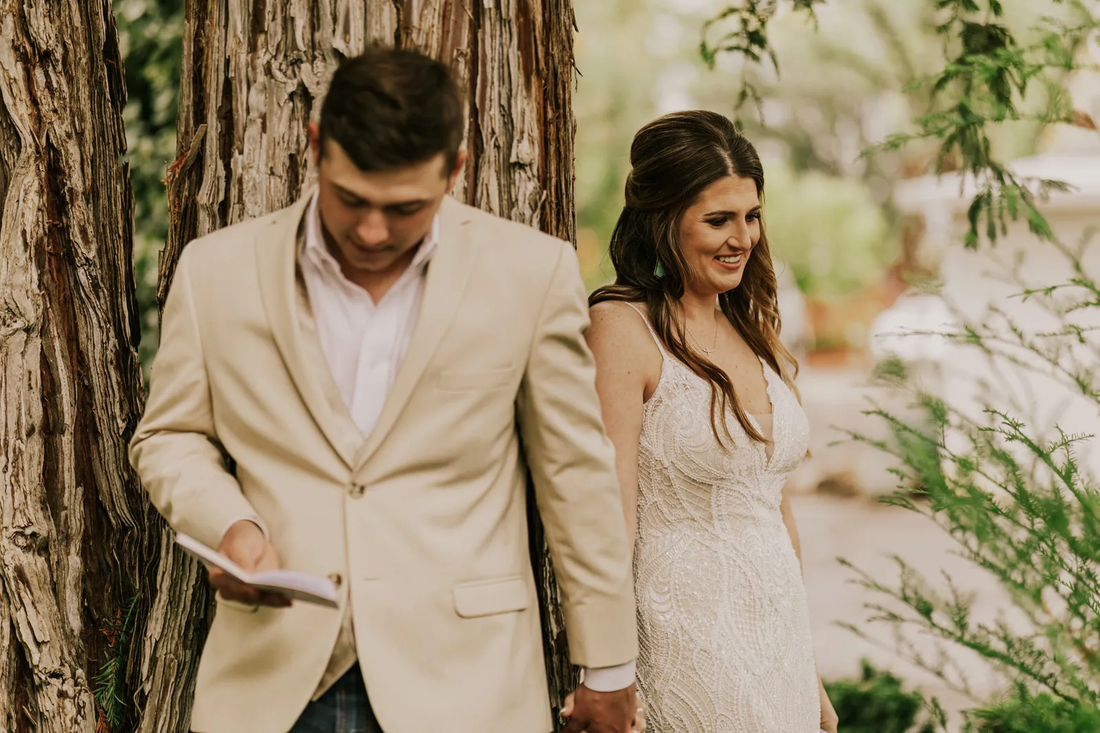 Bride and groom holding hands behind a tree as they read their vows in private.