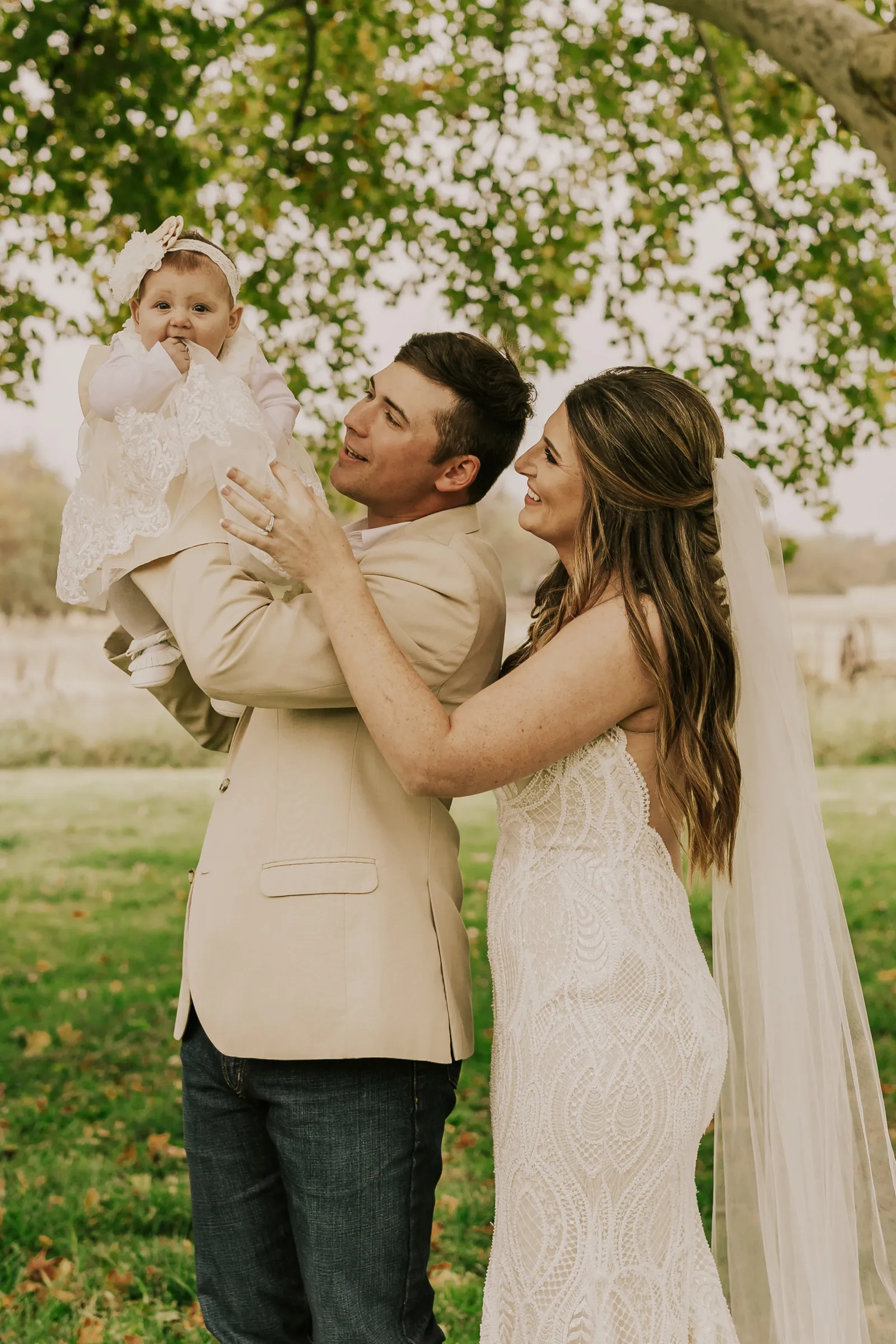 Bride and groom holding a baby in the air and smiling.