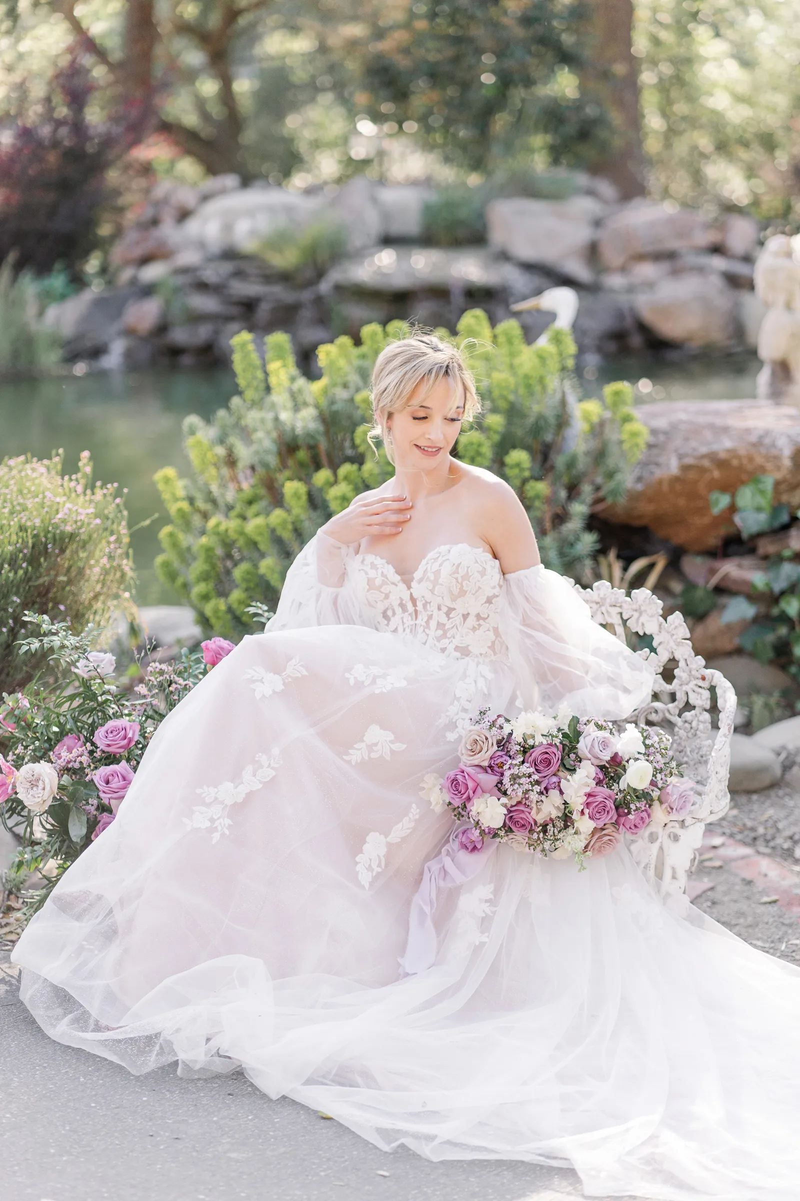 Blonde bride posing on a bench near an outdoor pond.