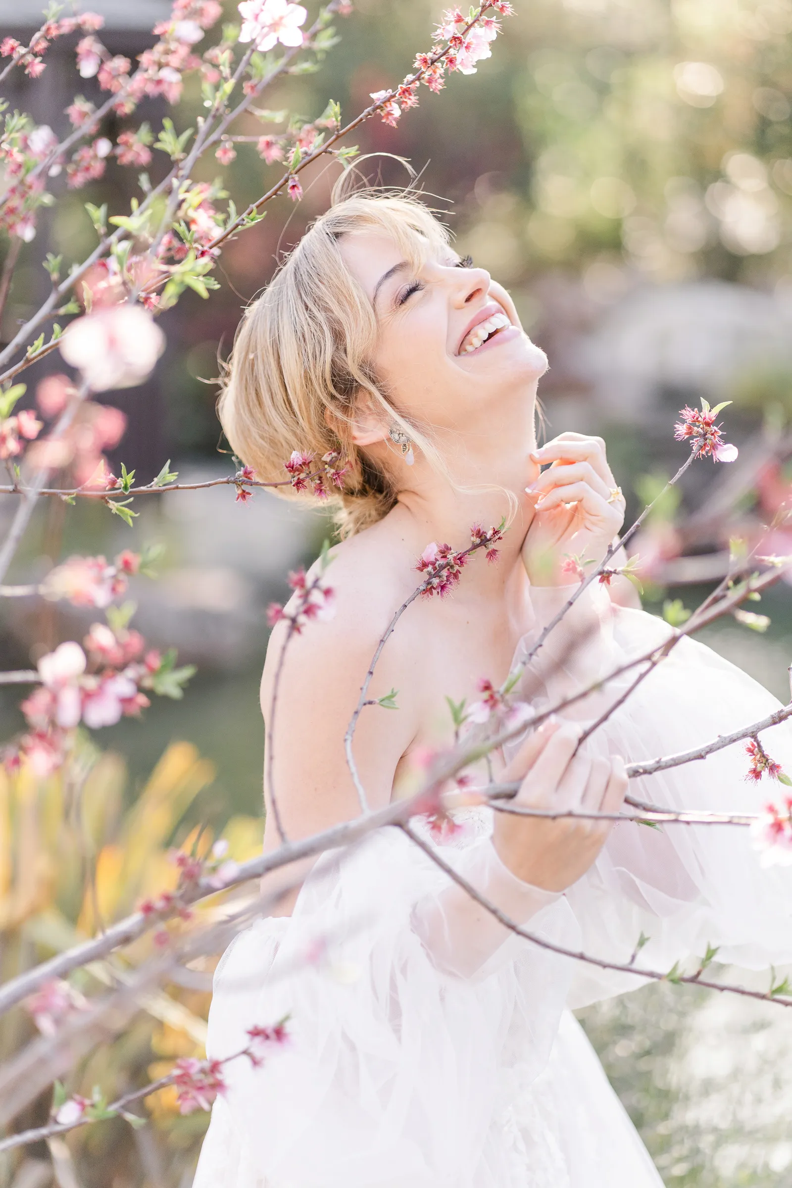 Bride laughing behind a cherry blossom tree.