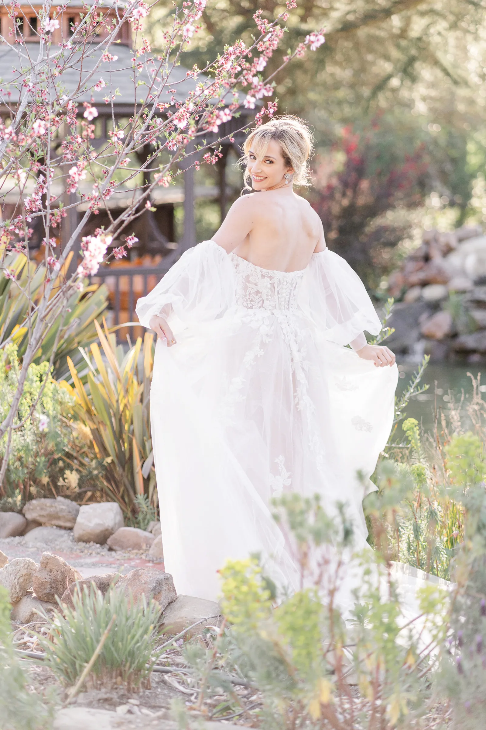 Full body photo of a bride twirling her dress by a cherry blossom tree.