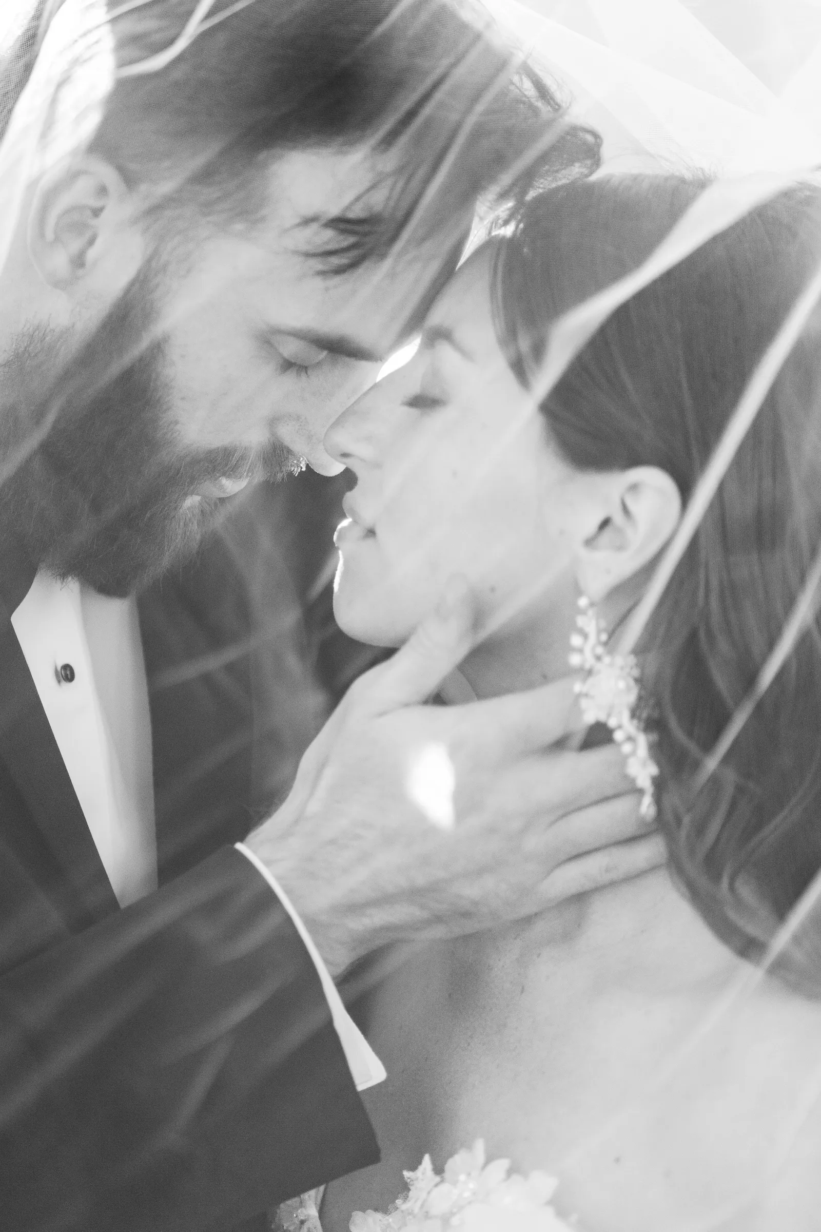 Black and white photo of a groom and bride touching foreheads inside the veil.