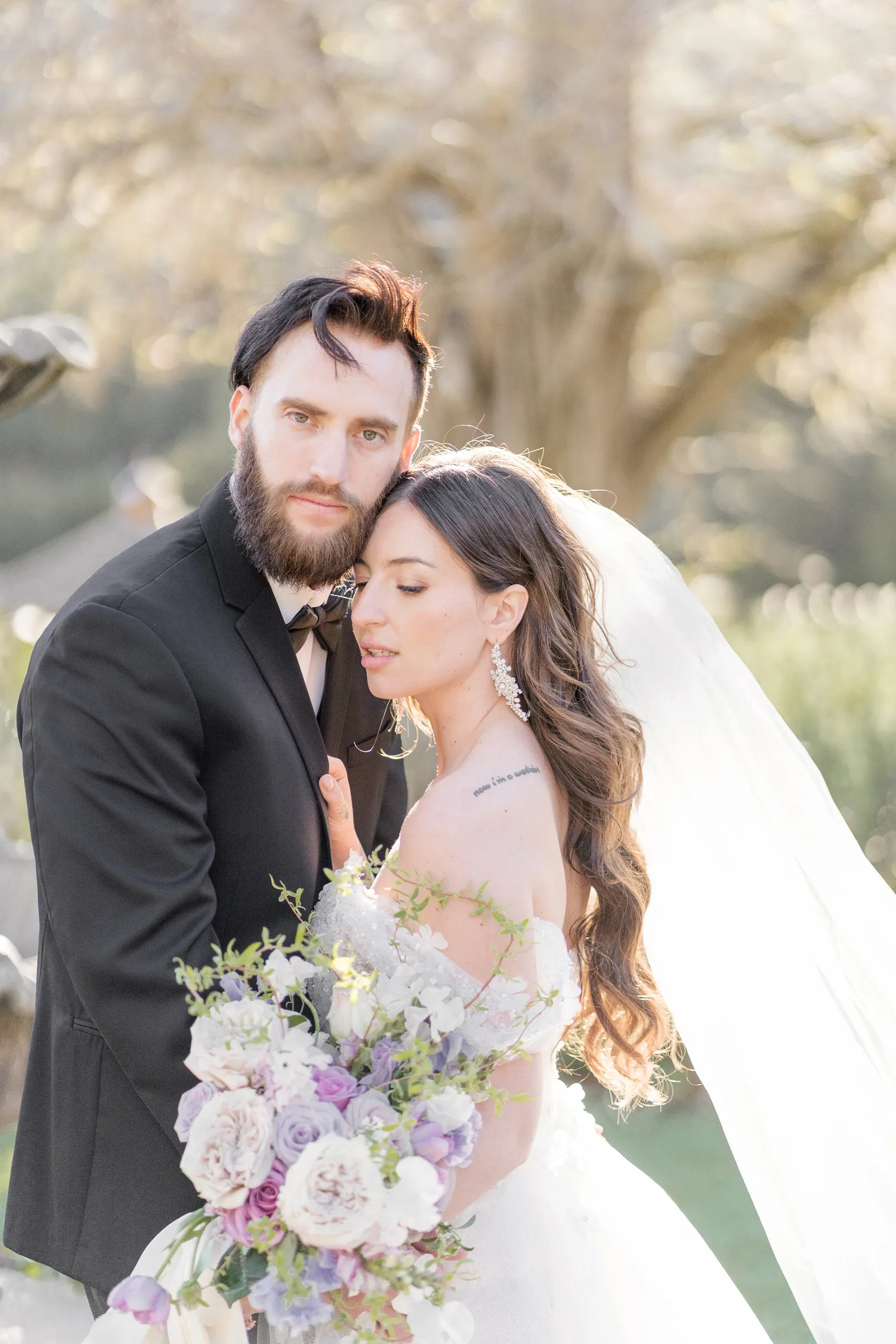 Bride leaning her head against her groom's chin as he looks into the camera.