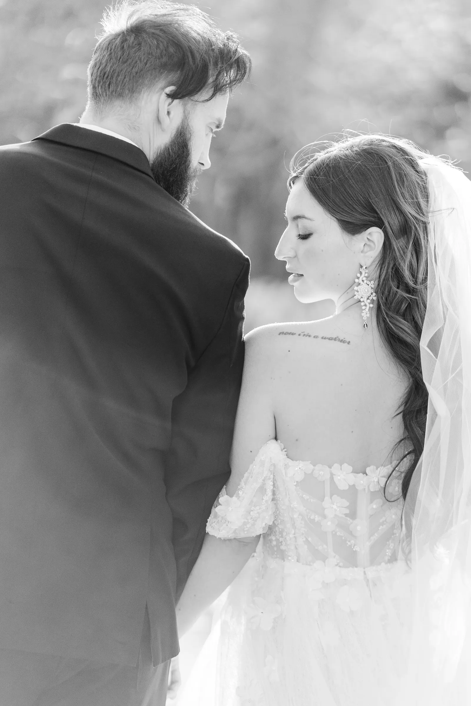 Black and white photo from behind of the bride and groom holding hands.