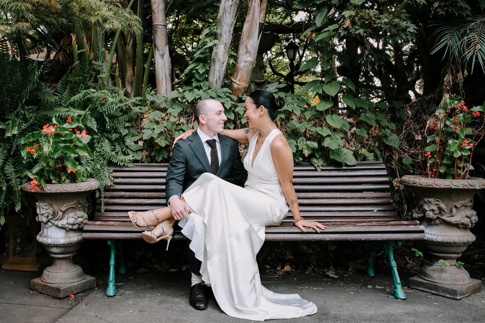 Bride sitting on a bench with her legs hanging over her groom's lap.