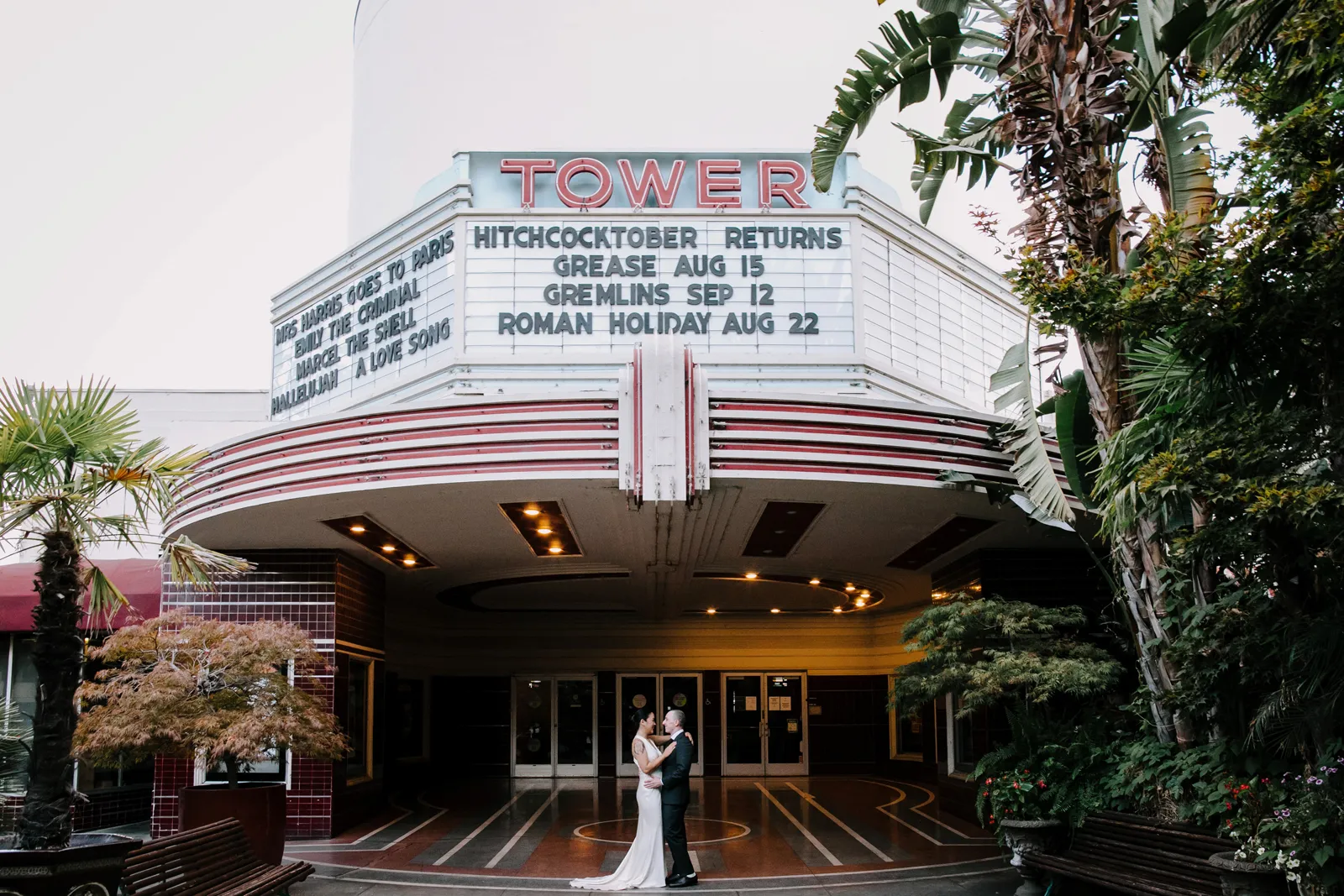 Bride and groom standing in front of the Tower theatre and holding hands.